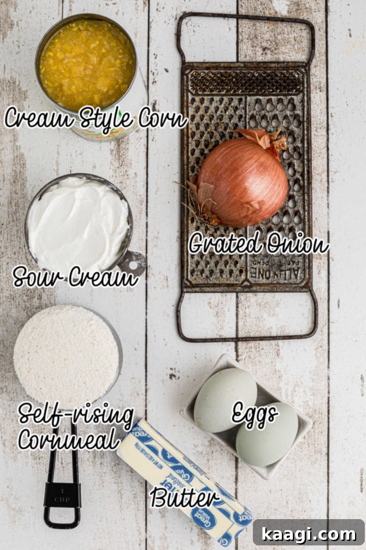 Overhead shot of the ingredients needed to make sour cream cornbread, including sour cream, cornmeal, eggs, butter, canned cream style corn, and a grated onion.
