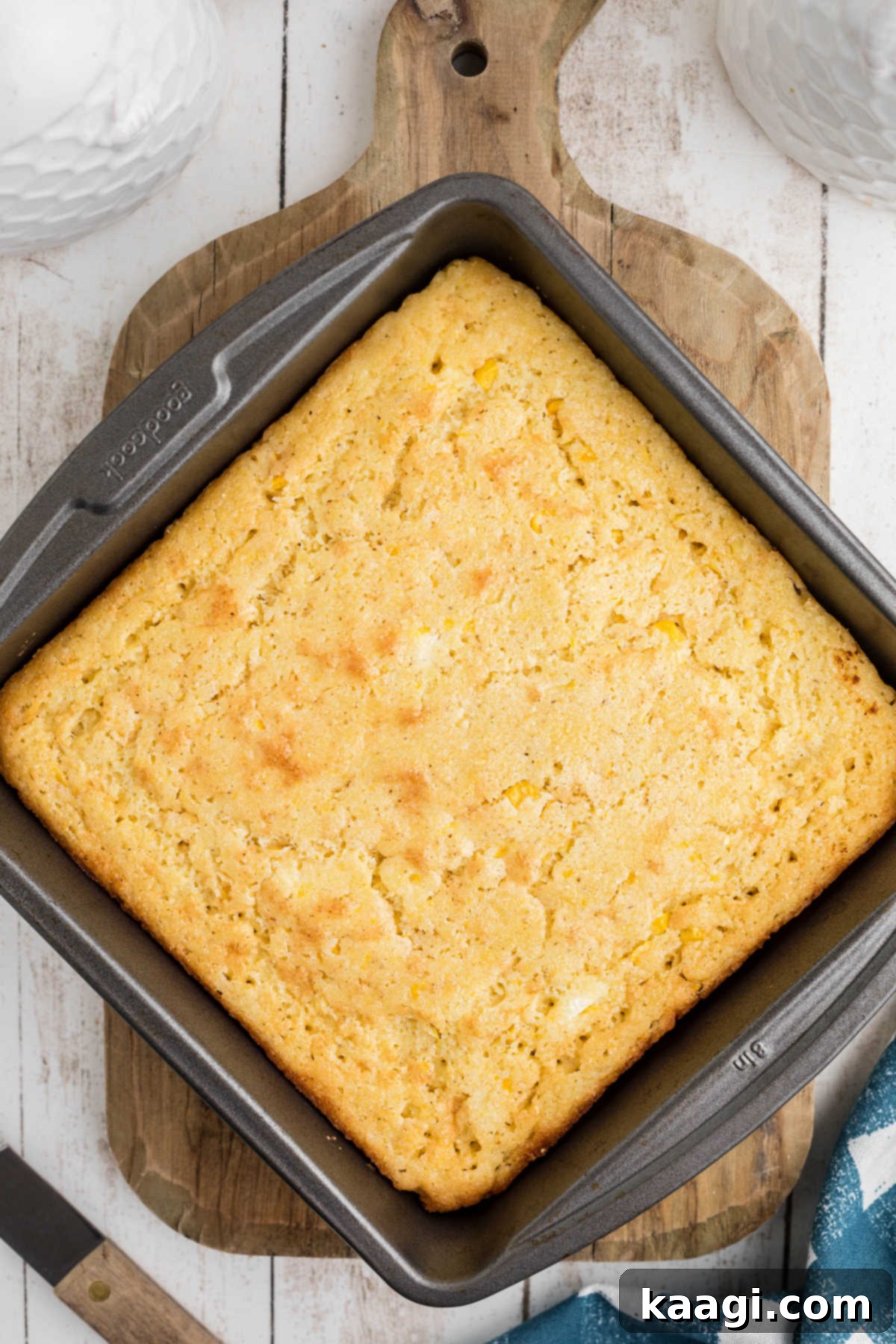 Overhead shot of a square cornbread, cooked in a baking pan, resting on a rustic wooden board.