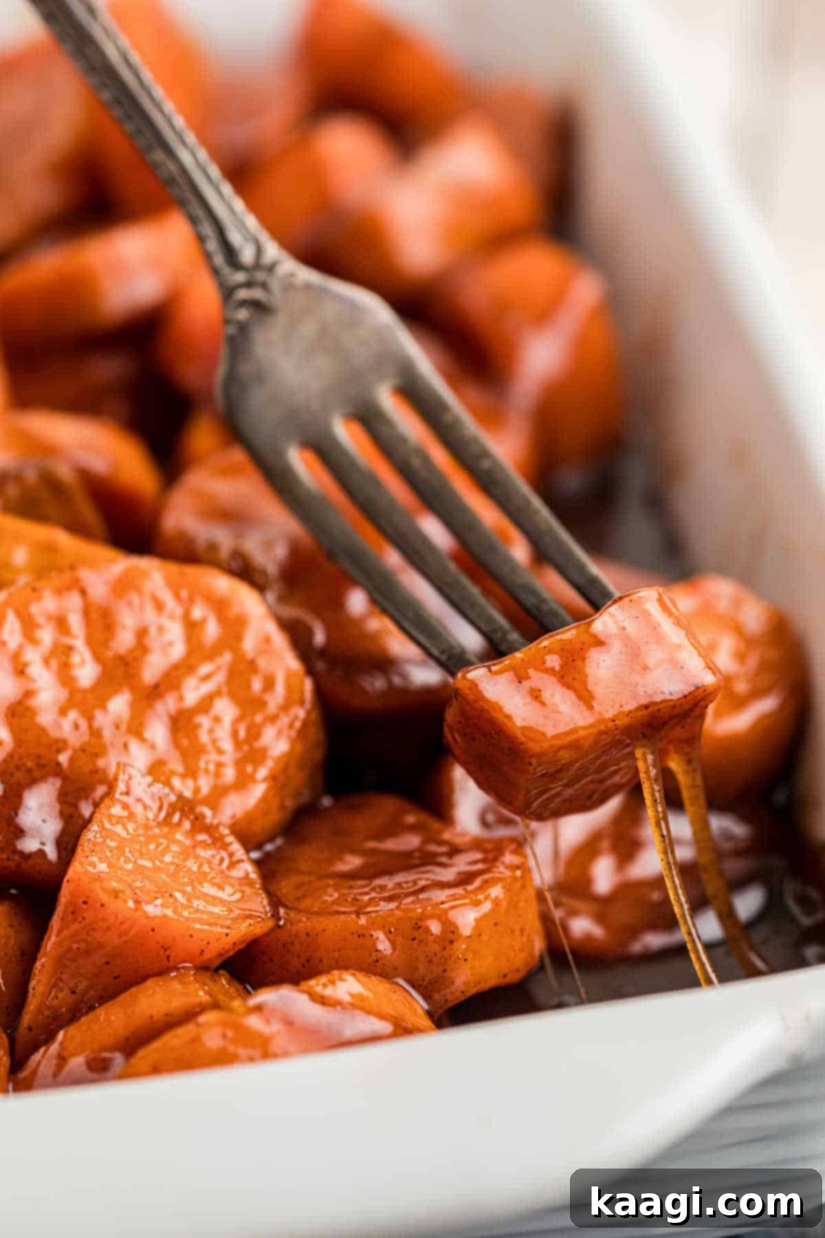 A fork digging into a dish full of candied yams, a gooey sticky treacle oozing down.