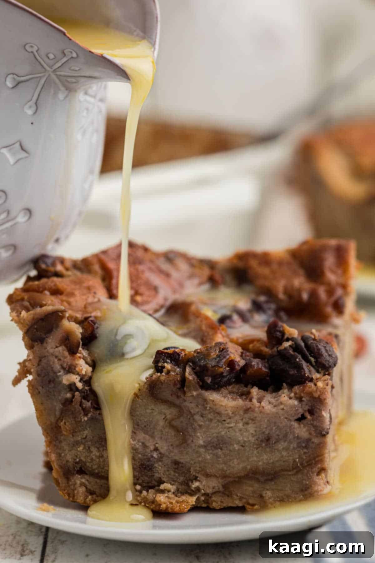 A slice of bread pudding on a plate with some rum sauce being poured over the top, garnished with toasted pecans.