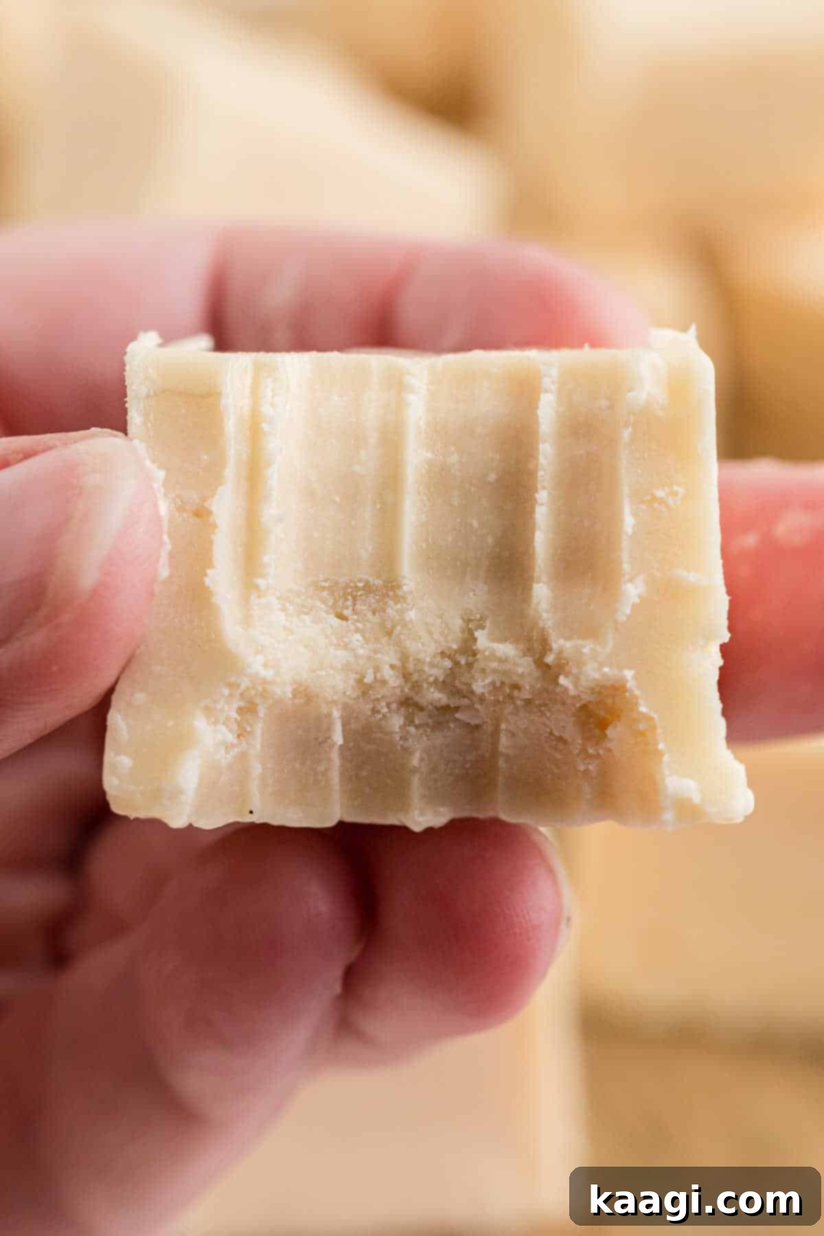 Close up of a piece of vanilla fudge with a bite taken out, showing its smooth interior.