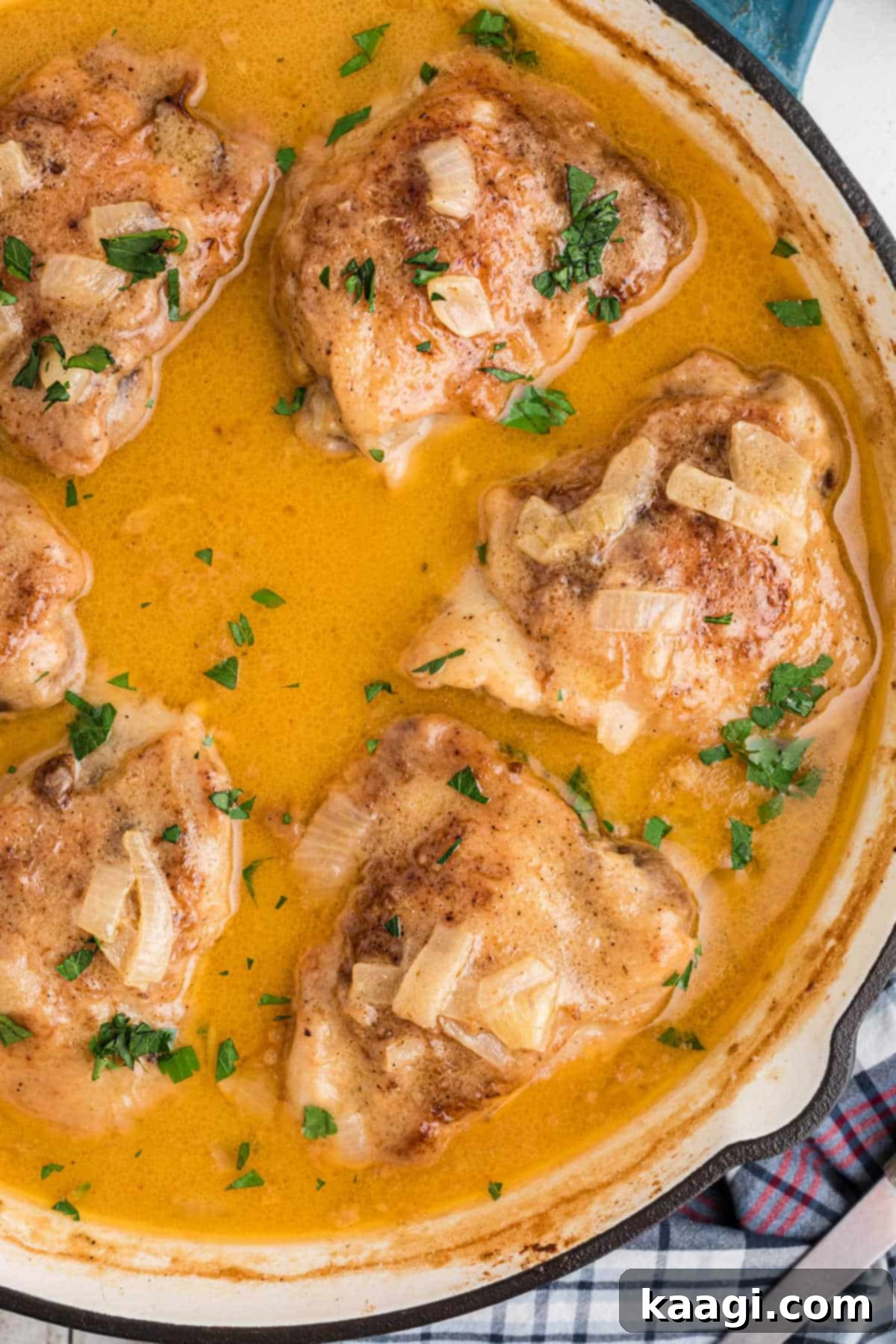 Overhead view of a beautiful skillet of smothered chicken, showing the golden-brown chicken thighs in a rich, creamy sauce, garnished and ready to serve.