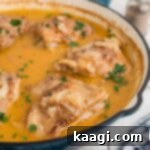 Side view of a rustic cast iron skillet with golden-brown smothered chicken thighs resting in a creamy, rich gravy, ready to be served.