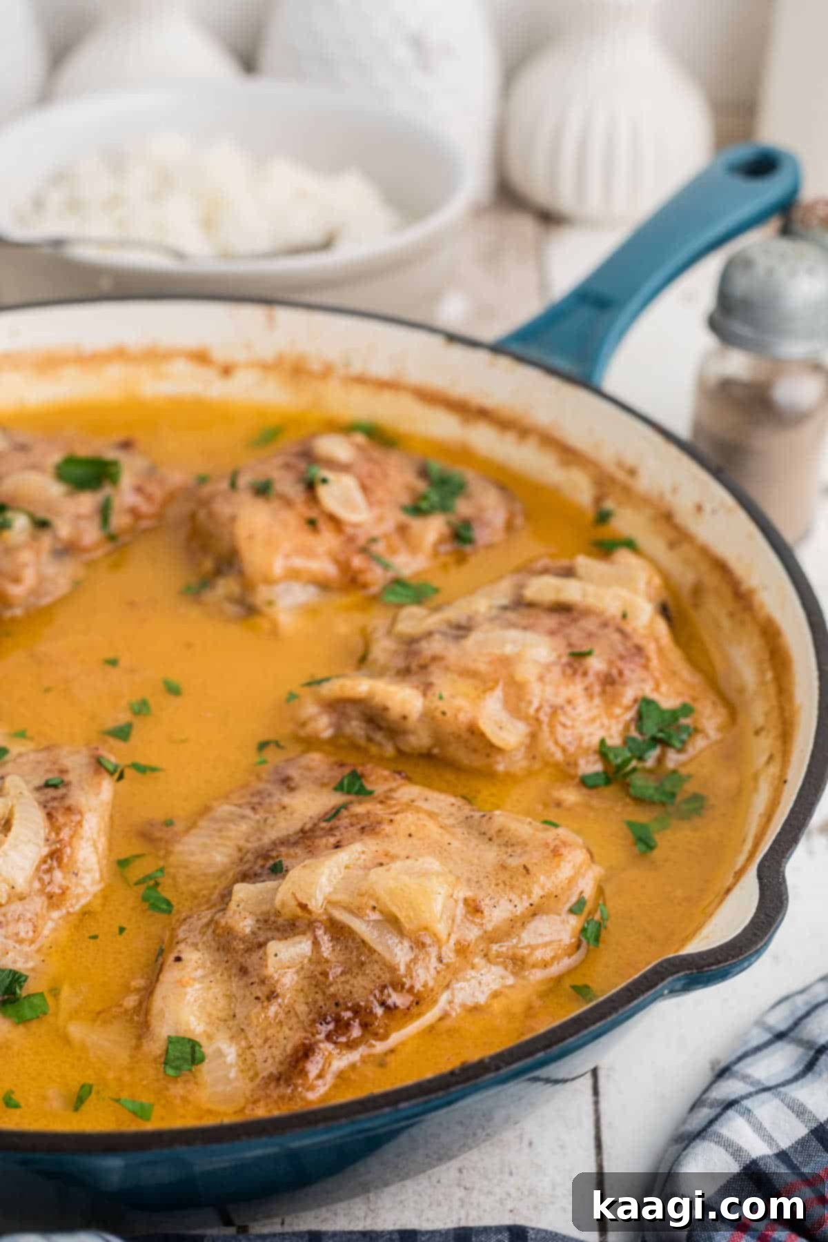 Side view of a rustic cast iron skillet filled with golden-brown smothered chicken thighs swimming in a rich, creamy gravy, ready to serve.