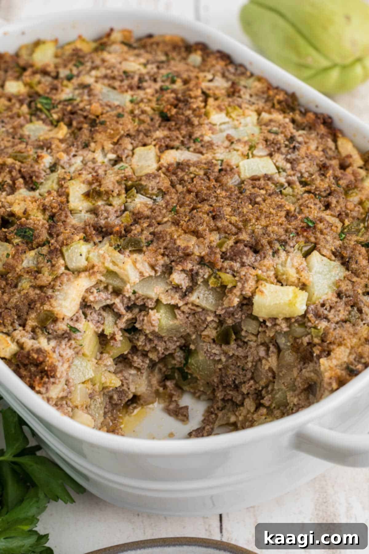 A casserole dish full of chayote dressing, golden brown and garnished.