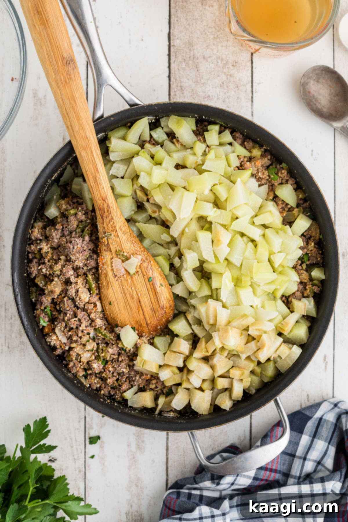 Chopped mirlitons being added to a large skillet containing the meat, vegetable, and breadcrumb mixture.