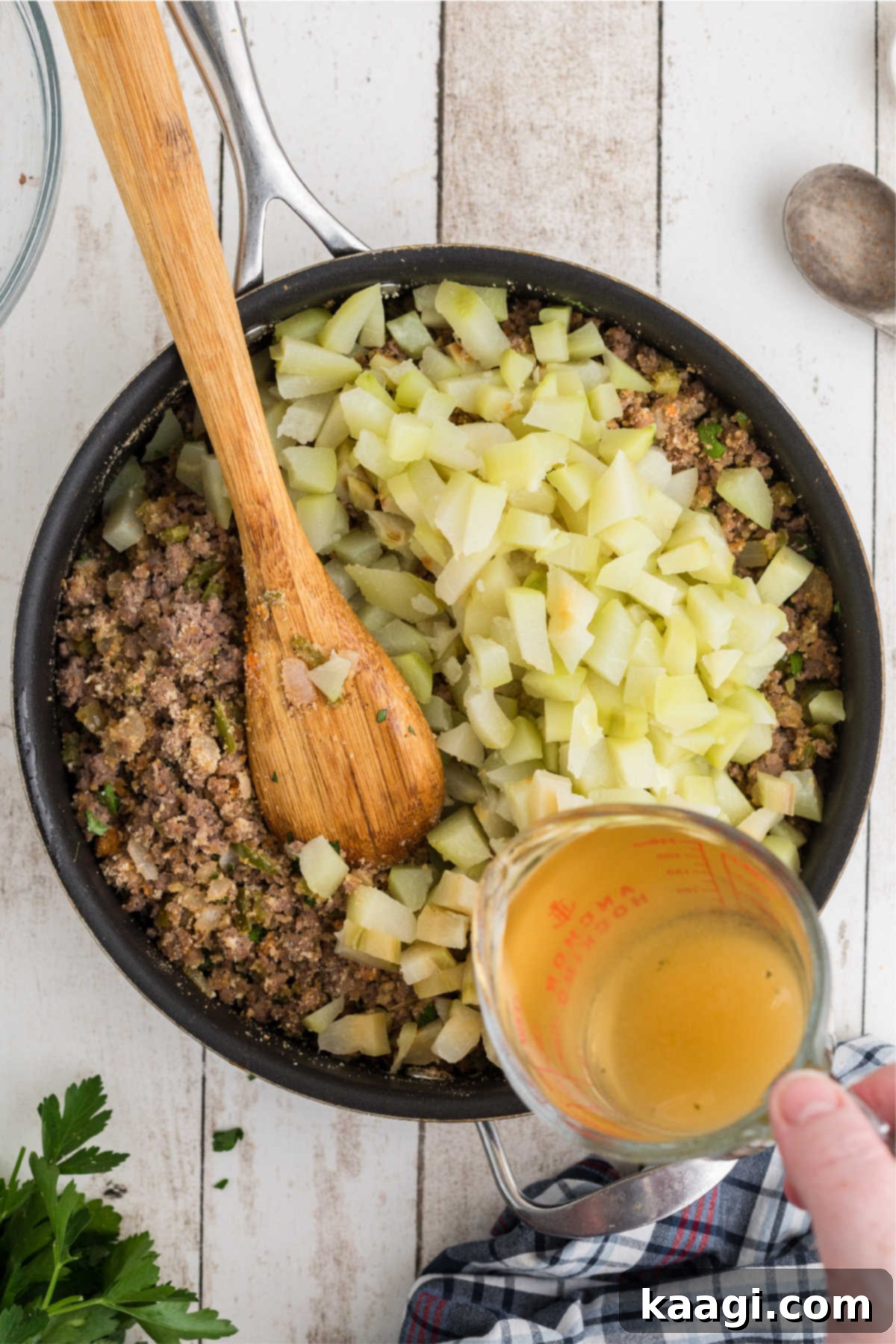 Chicken broth being poured into a skillet with mirlitons and other dressing ingredients.