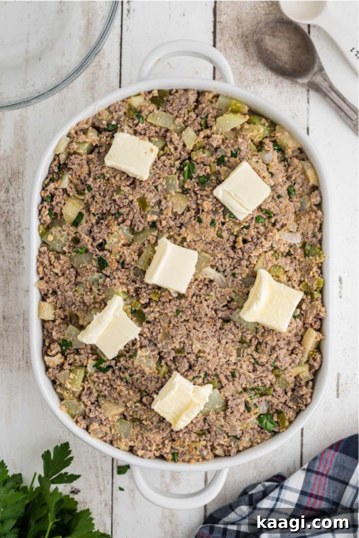 A baking dish filled with Mirliton dressing, topped with pats of butter, ready for the oven.