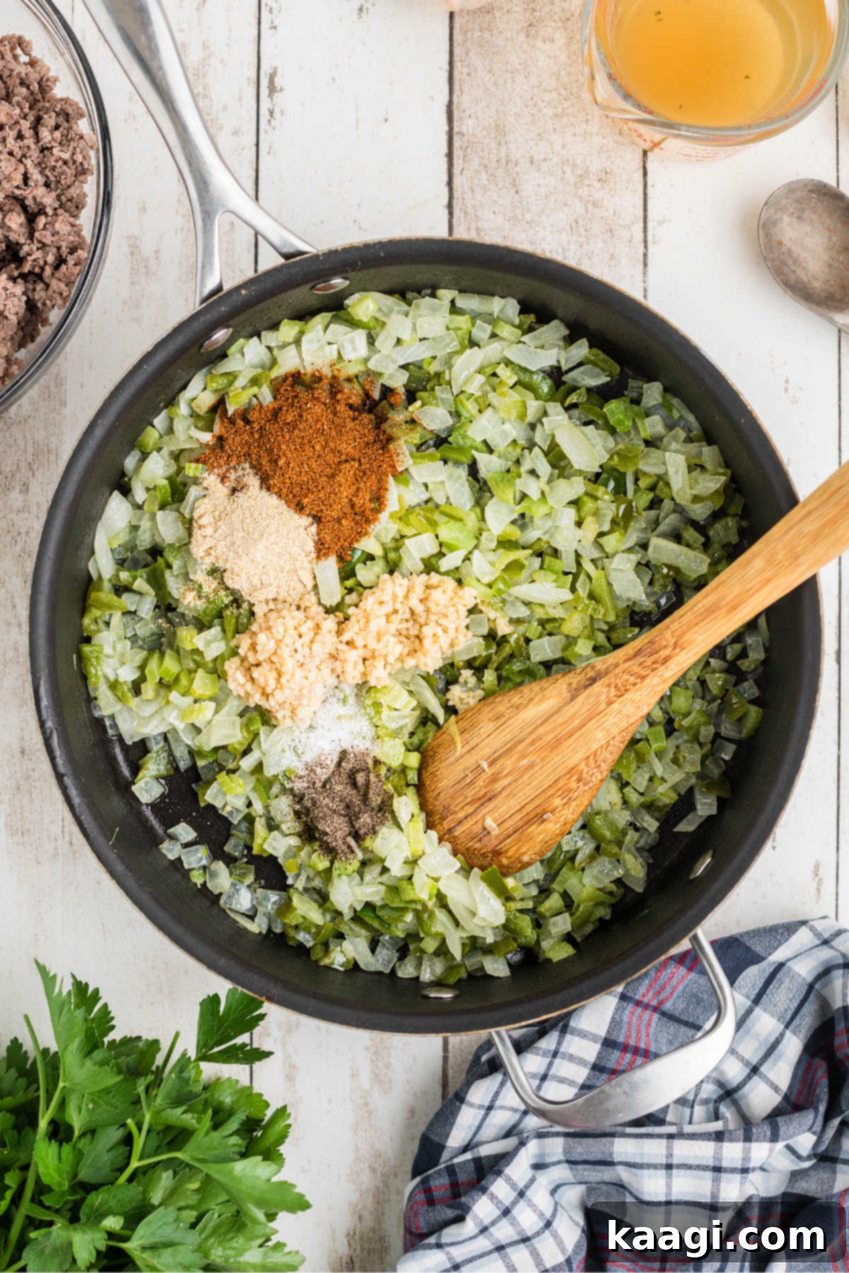 Minced garlic and various seasonings being added to the cooked vegetables in the pan.