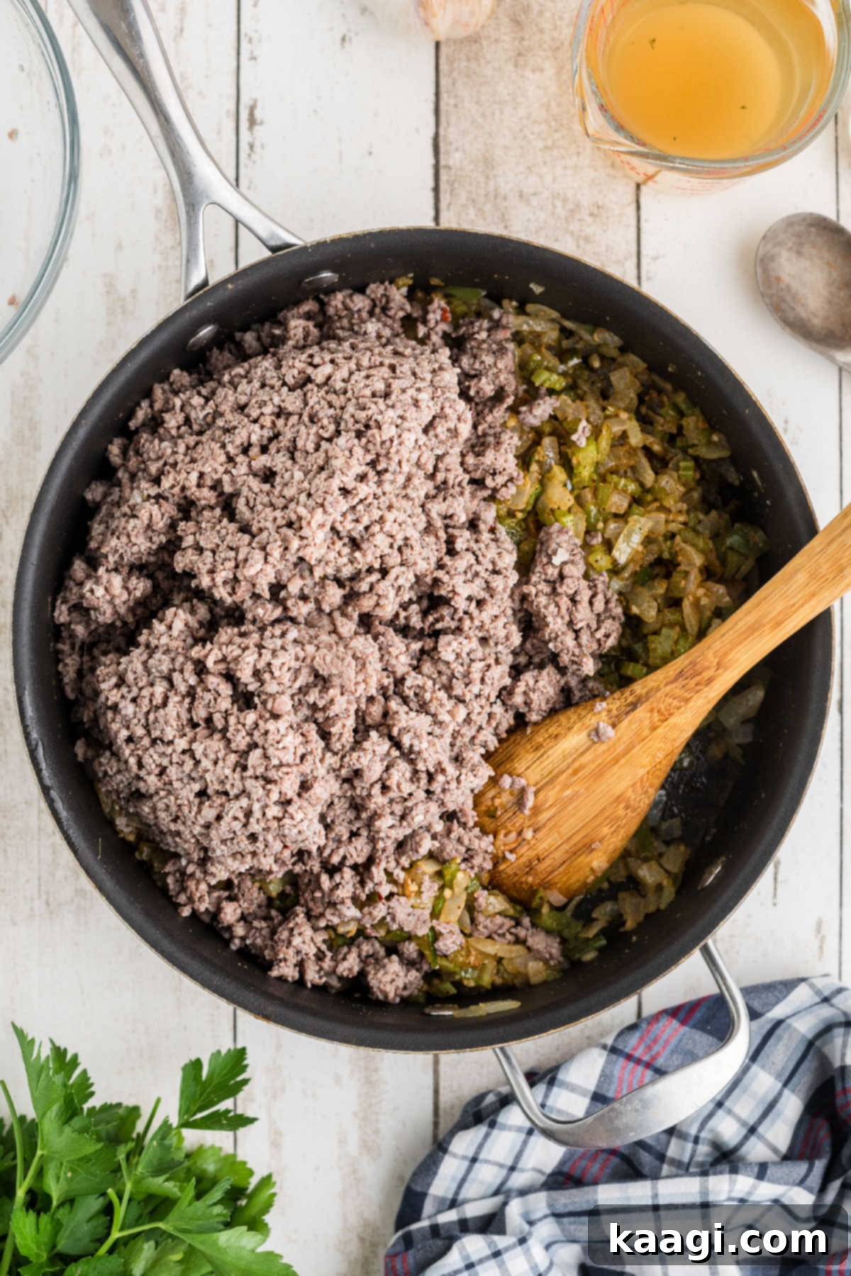 The browned ground meat being added back into the skillet with the sautéed vegetables.