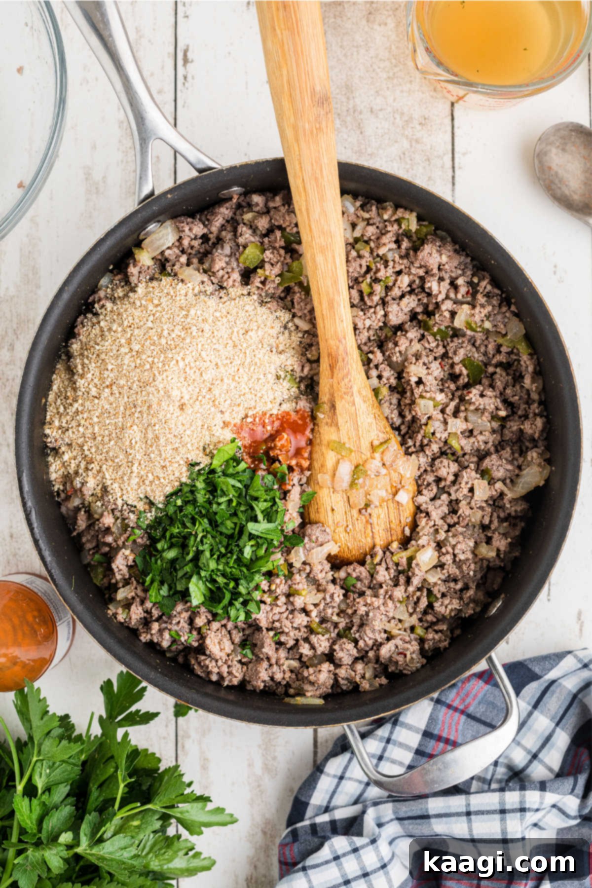 Plain breadcrumbs, chopped parsley, and hot sauce being added to the meat and vegetable mixture.