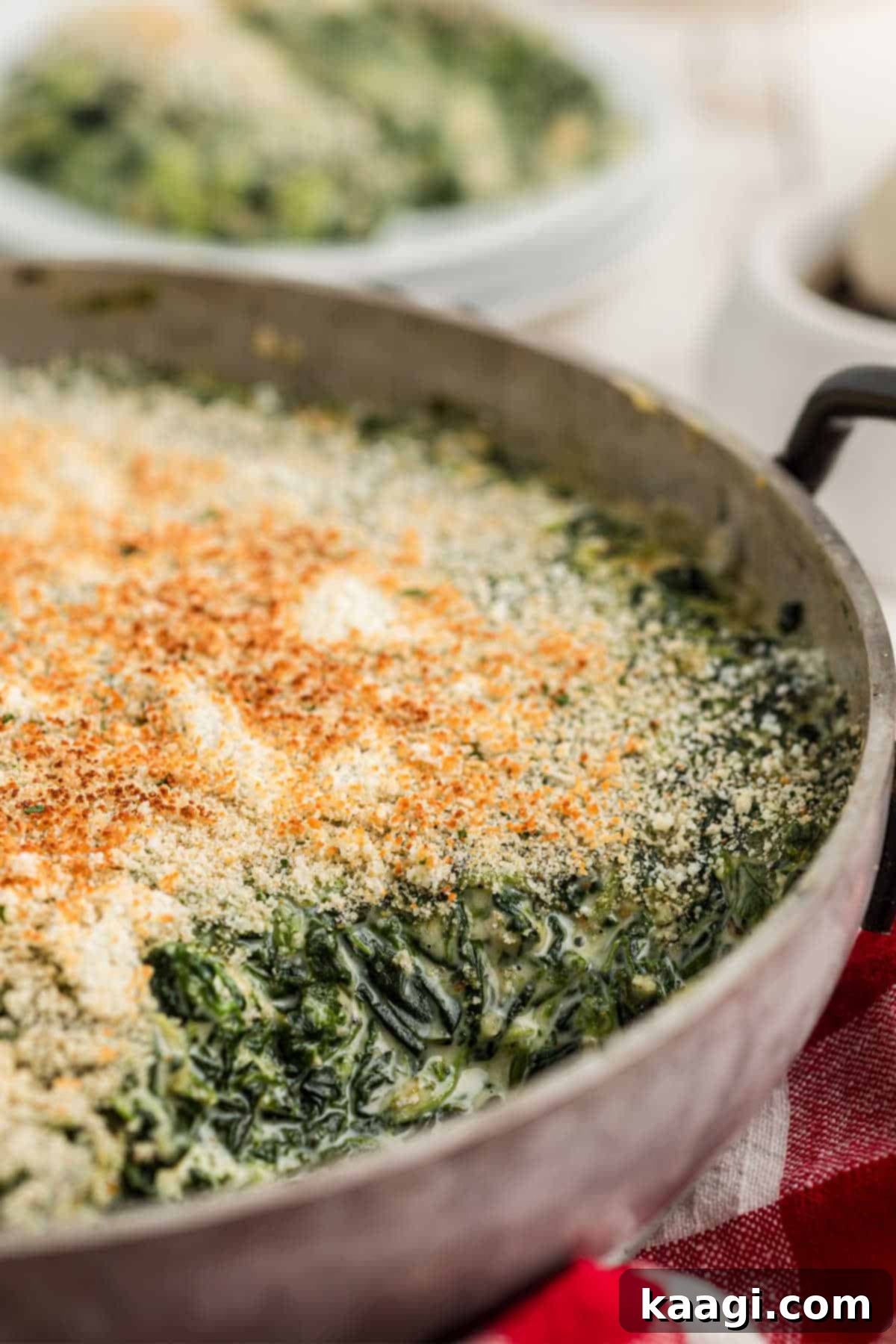 A delectable pan of creamy Spinach Madeleine with a scoop missing, showcasing its rich texture and golden crumb topping.
