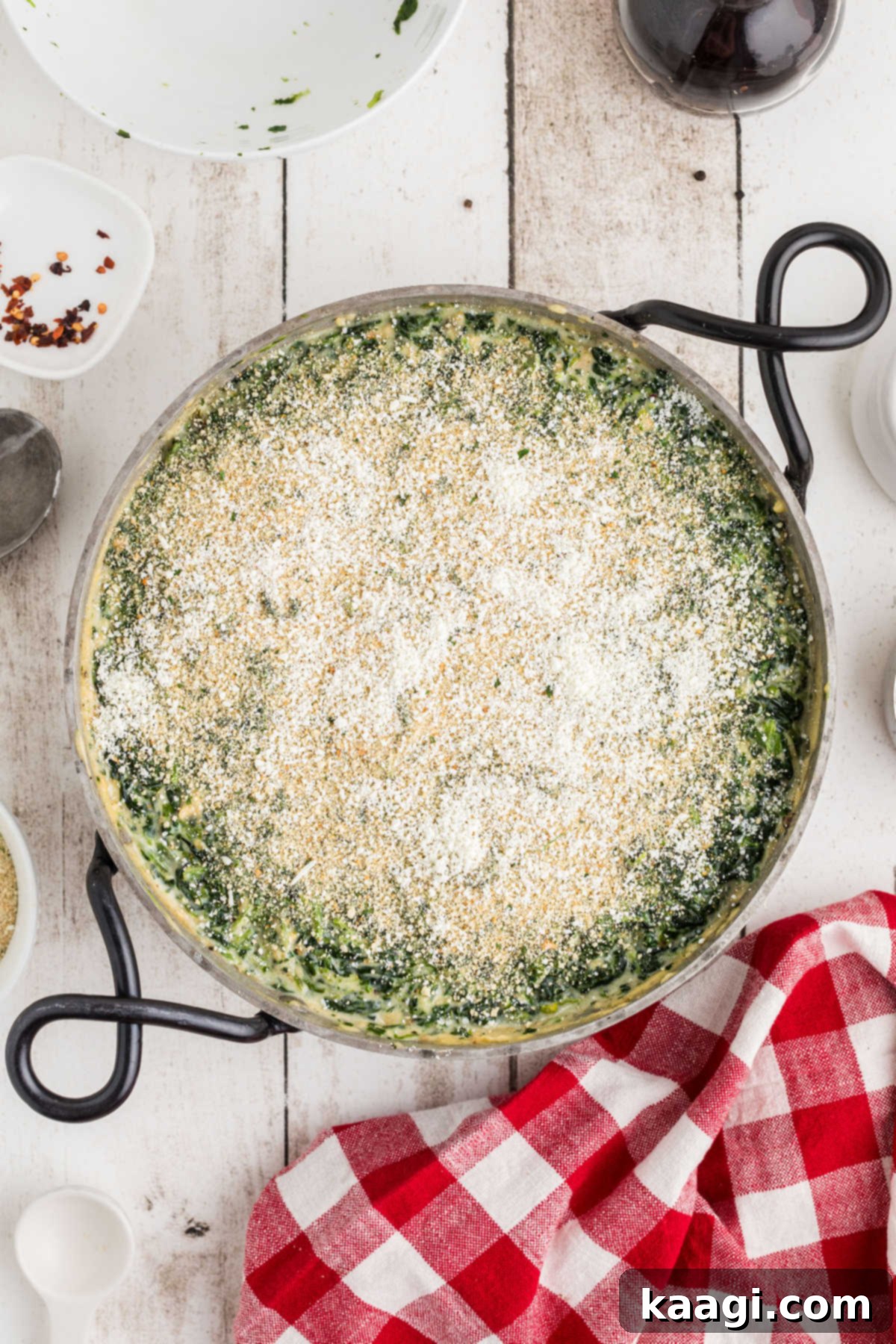 Breadcrumb and parmesan cheese mixture being sprinkled evenly on top of the spinach dish in a skillet.