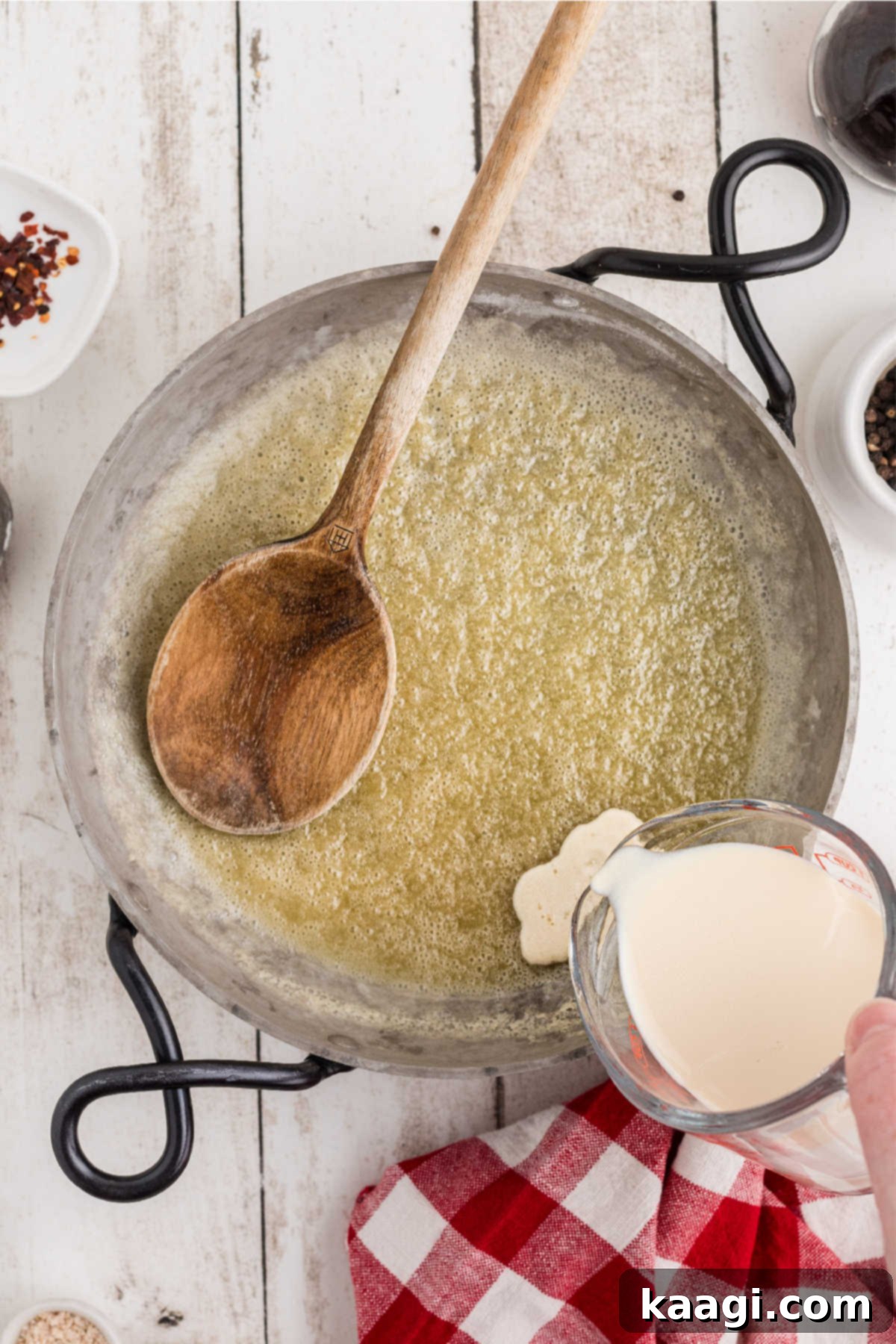 Evaporated milk being slowly poured into a skillet containing the cooked butter and flour roux, ensuring a smooth consistency.