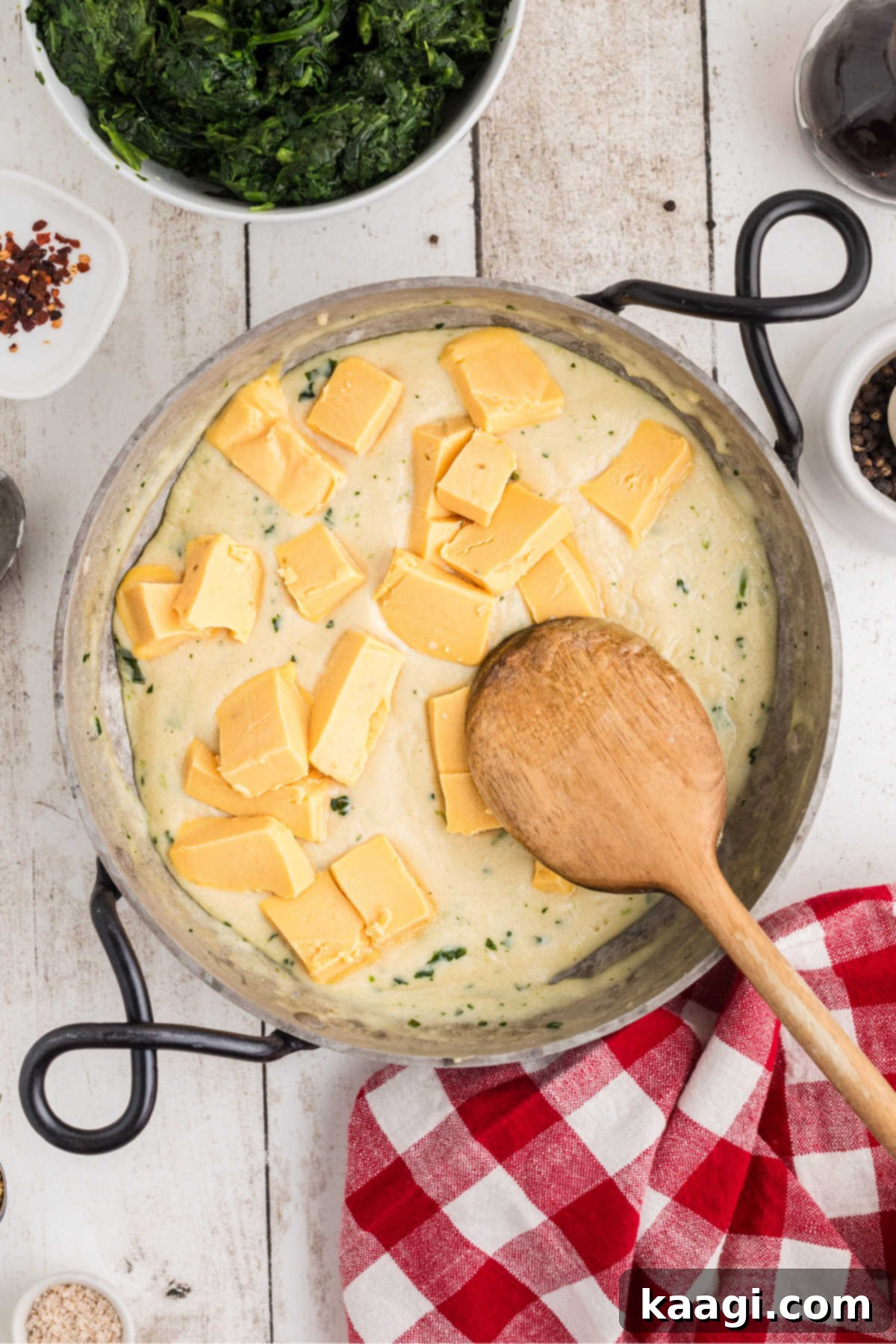 Cubed Velveeta cheese being added to a skillet with a simmering roux and milk mixture.