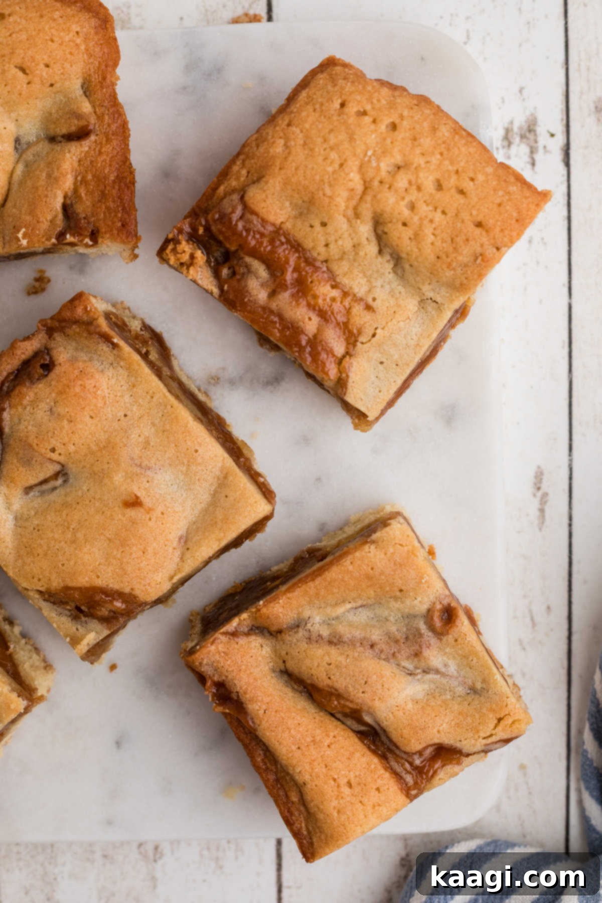 Caramel-Swirled Blondie Squares 6 An overhead close-up shot of several perfectly cut caramel blondies arranged on a elegant granite plate, highlighting their gooey centers and golden-brown tops.