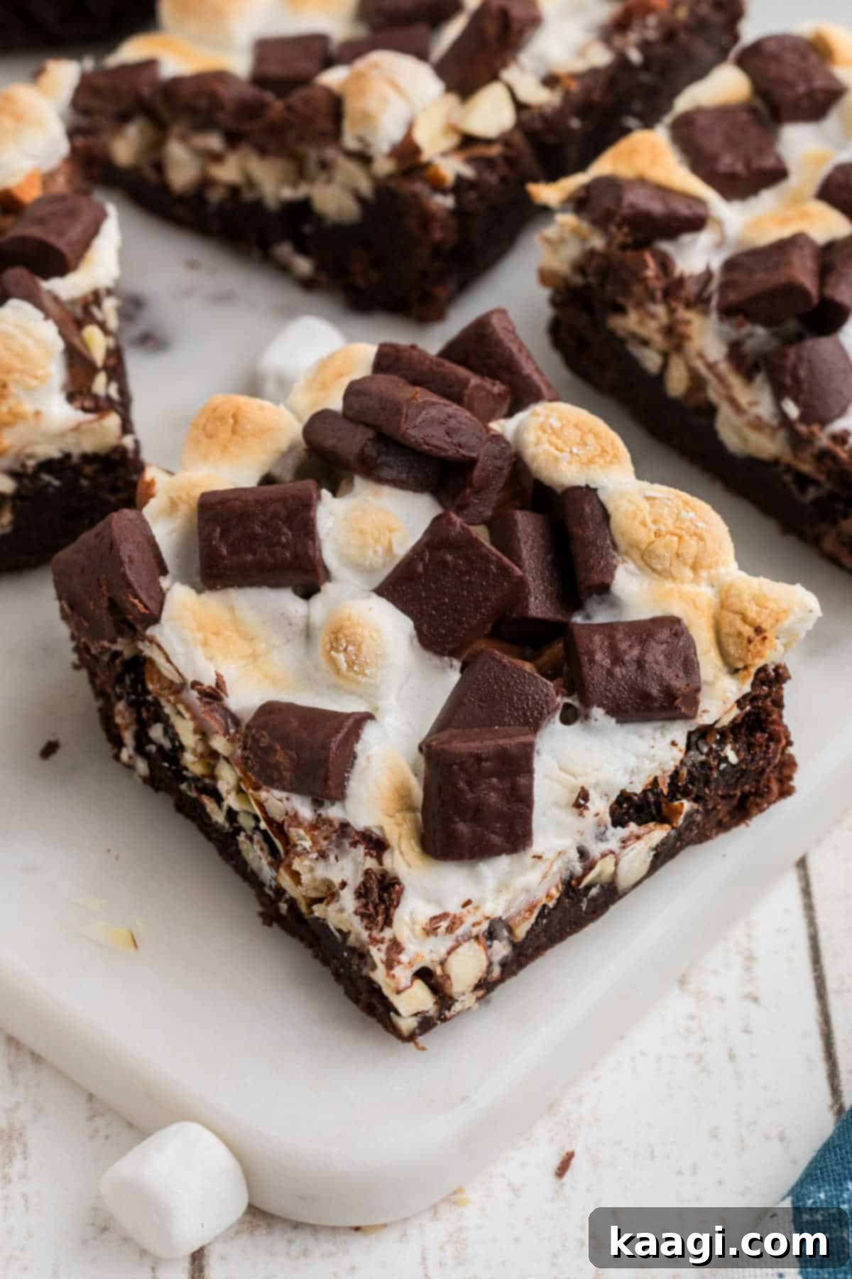 A delectable close-up shot of a single rocky road brownie square, showcasing its fudgy interior, melted marshmallows, and crunchy nuts, resting on a dark wooden board.