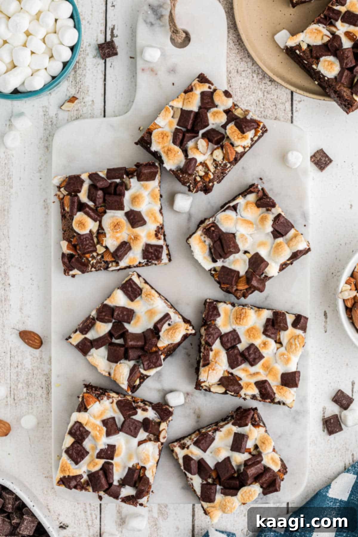An inviting overhead shot of perfectly cut rocky road brownies arranged neatly in squares on a dark wooden cutting board, ready to be served. The toppings of melted marshmallows and crunchy nuts are clearly visible.