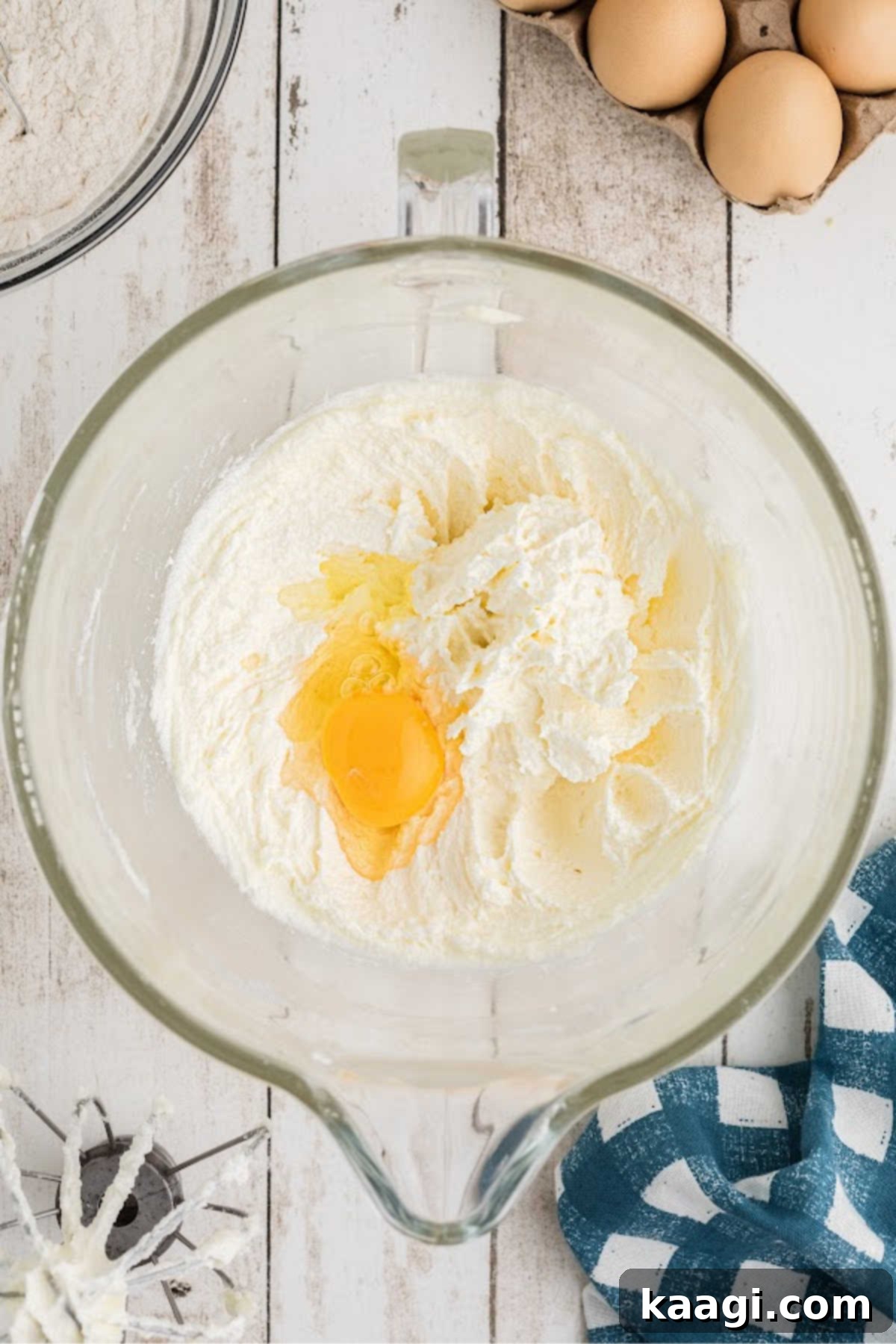 Eggs being added to a creamed butter and sugar batter, one by one.