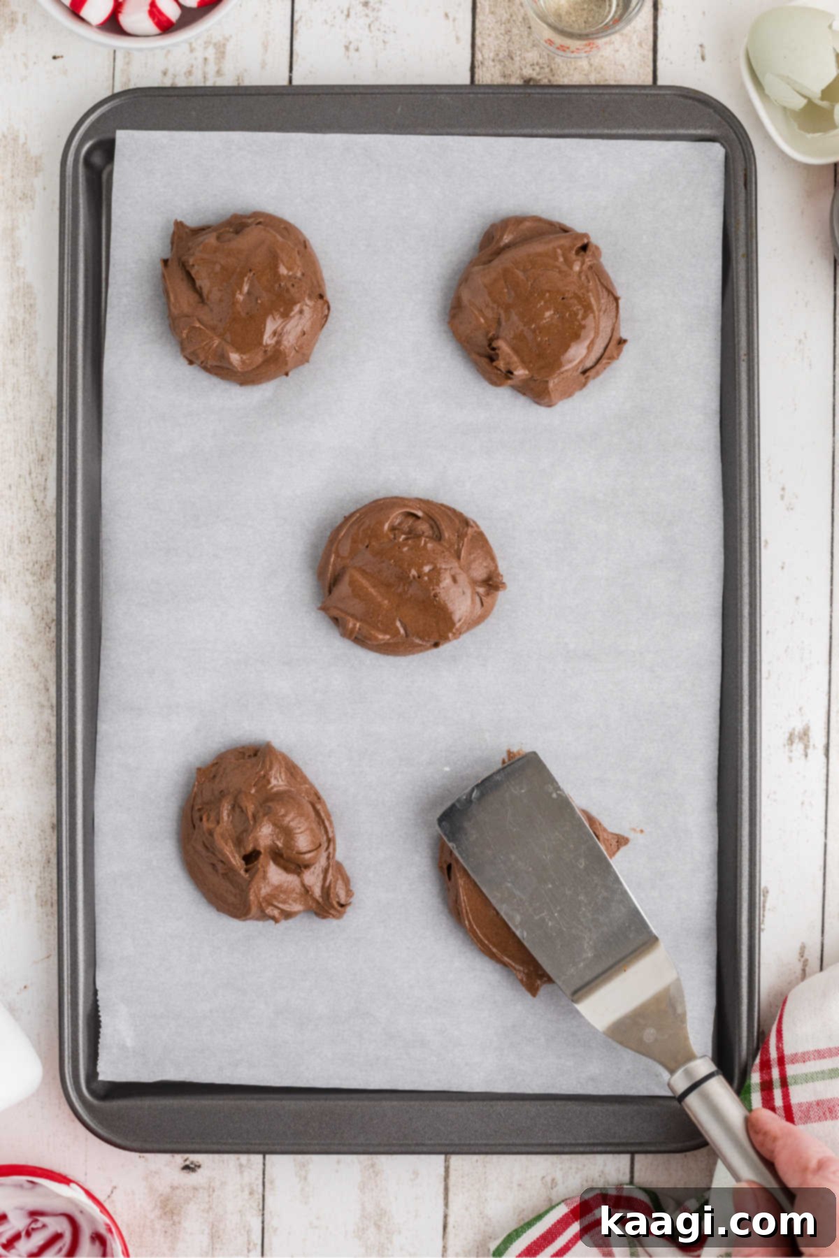 Cookie batter dropped onto a baking sheet then being flattened with a spatula.