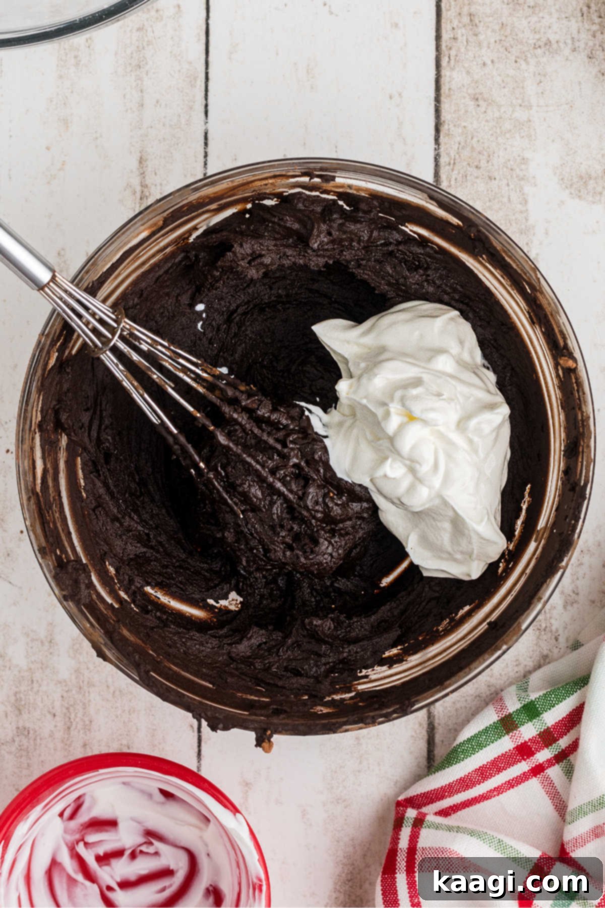 Sour cream added to a chocolate mixture in a mixing bowl.