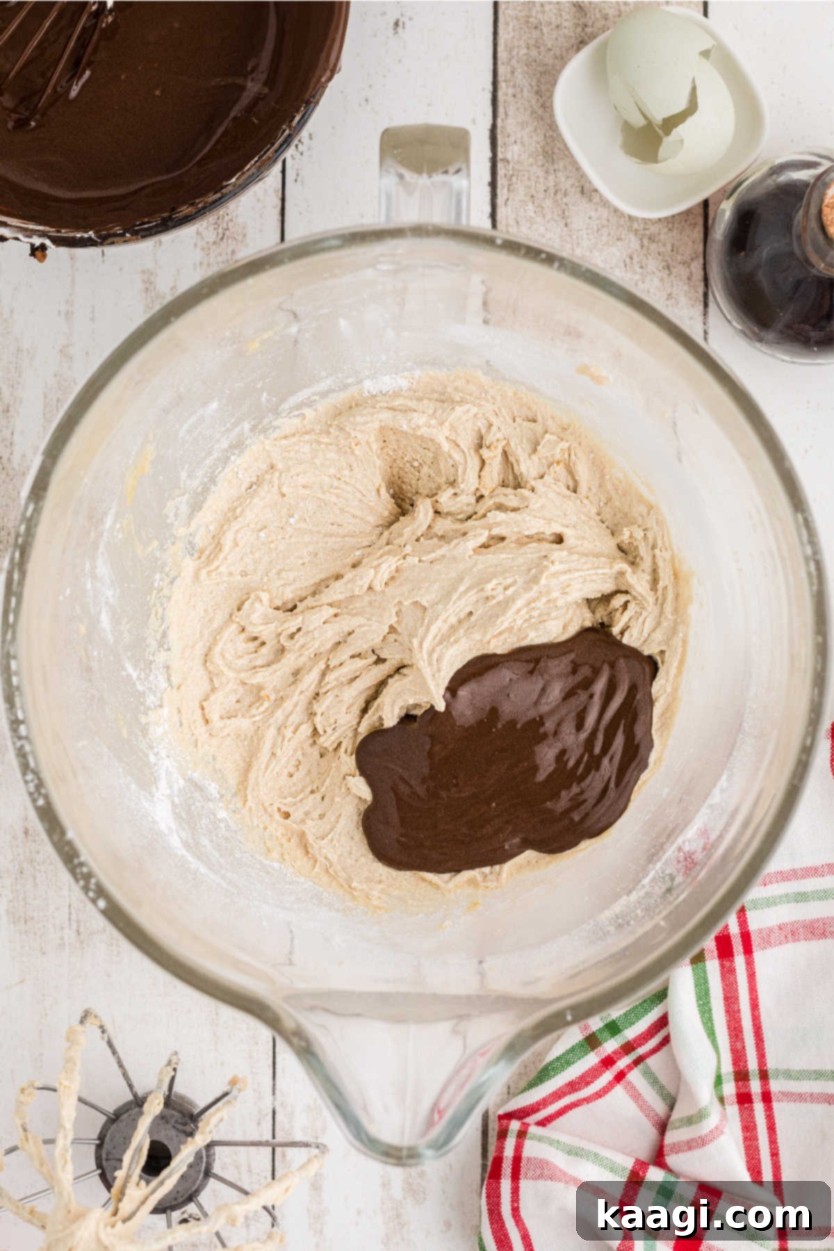A chocolate mixture being added to a mixing bowl with other ingredients.