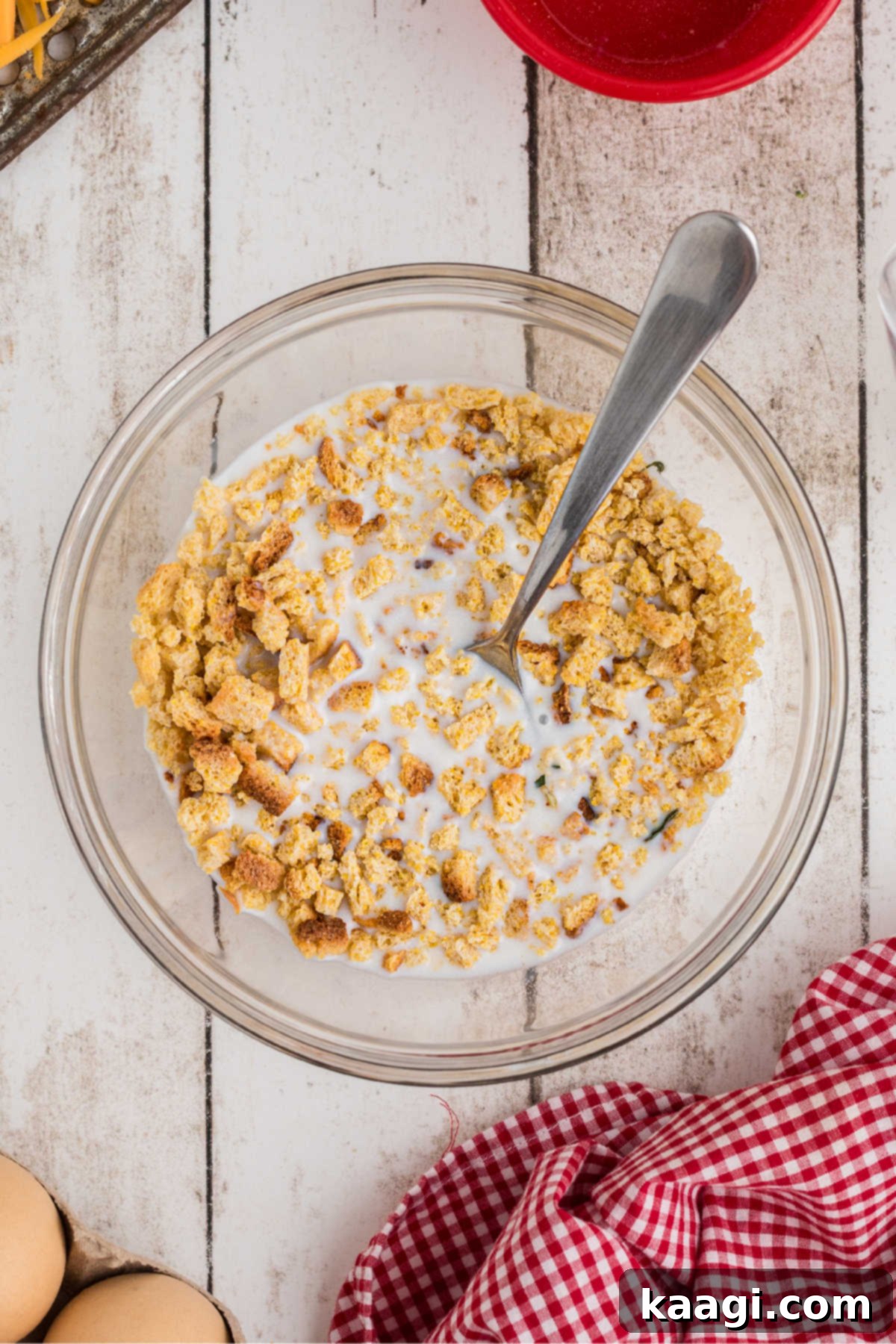 Golden Broccoli Bake 5 Cornbread stuffing mix soaking in a large mixing bowl with milk, being stirred with a fork, ready to absorb the liquid.