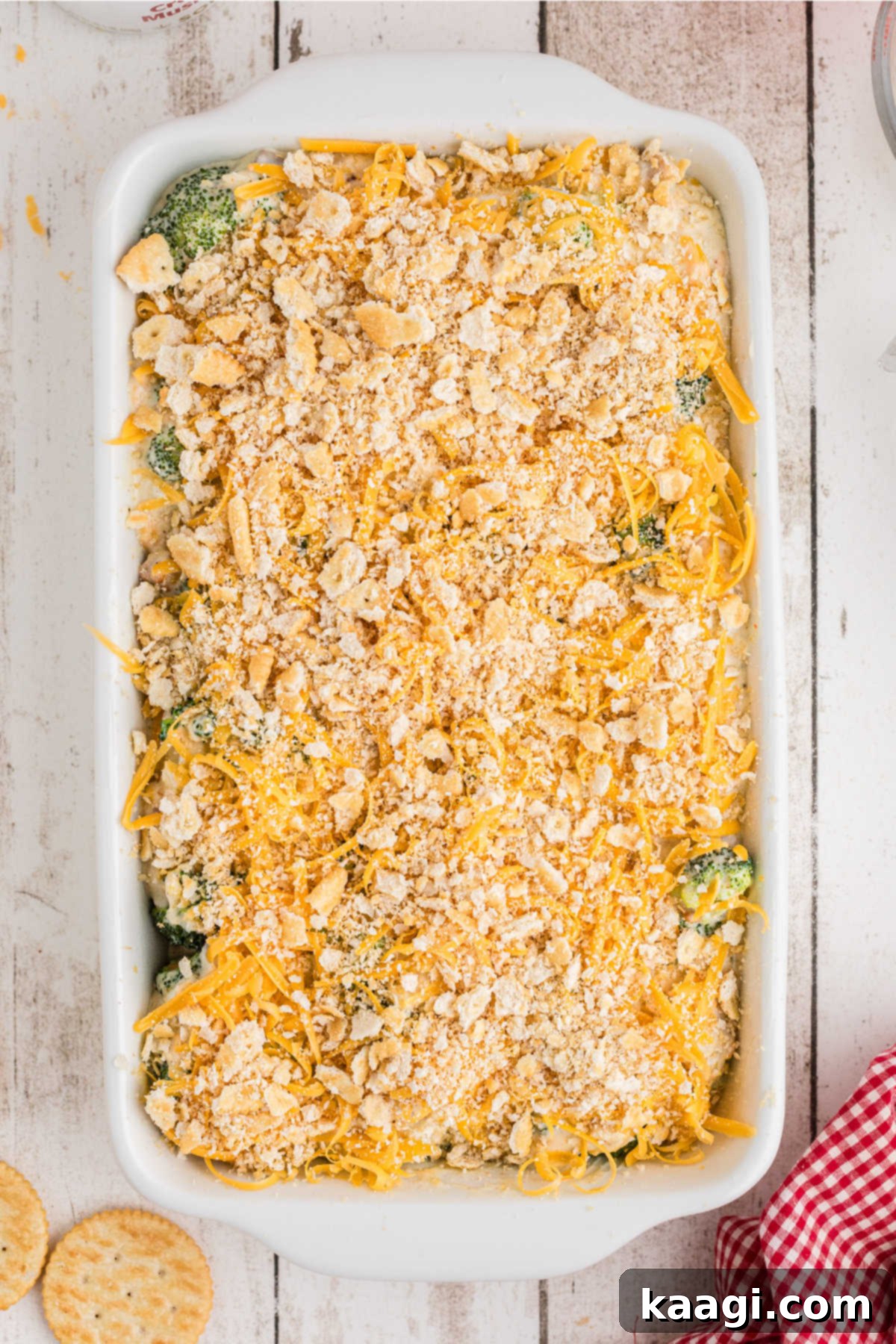 A broccoli casserole topped with remaining cheese and crushed cracker crumbs, ready for the oven.