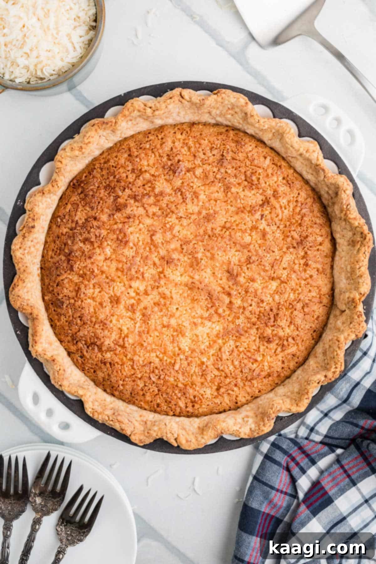 A beautifully baked old fashioned coconut pie, golden-brown and perfectly set, presented whole on a rustic blue and white ceramic plate.