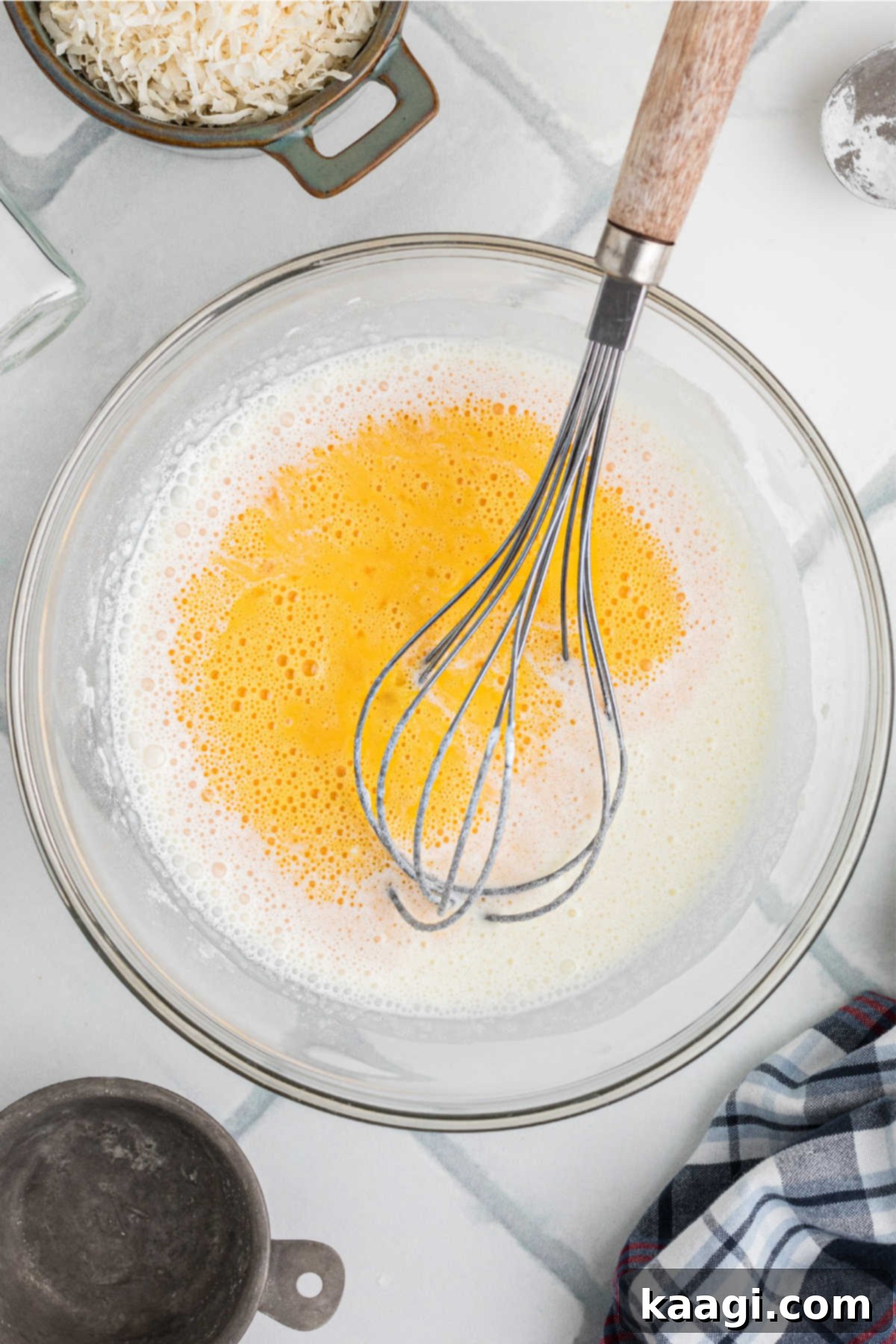 Beaten eggs, with their vibrant yellow yolk and white visibly mixed, are carefully poured into a large mixing bowl already containing sugar, cornstarch, and heavy cream, signifying the next stage of ingredient combination.