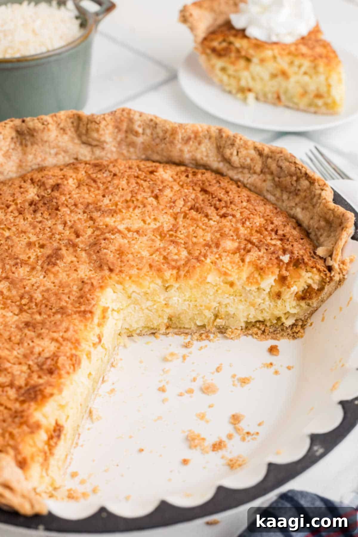 A freshly baked old fashioned coconut pie, with several slices already removed, revealing its creamy white interior and golden crust, presented on a rustic wooden board.