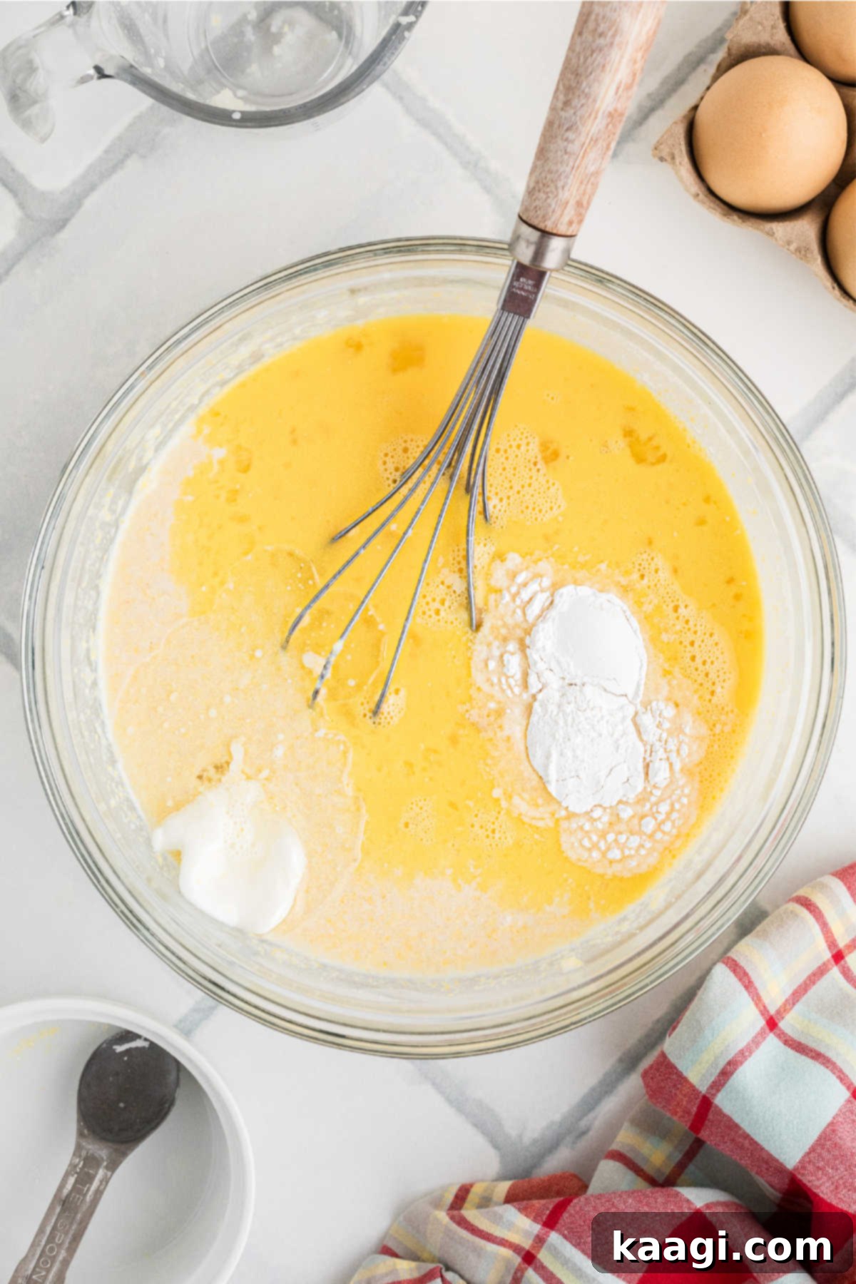 A large mixing bowl, filled with a spoon bread batter, with eggs, melted shortening, and baking powder already added.