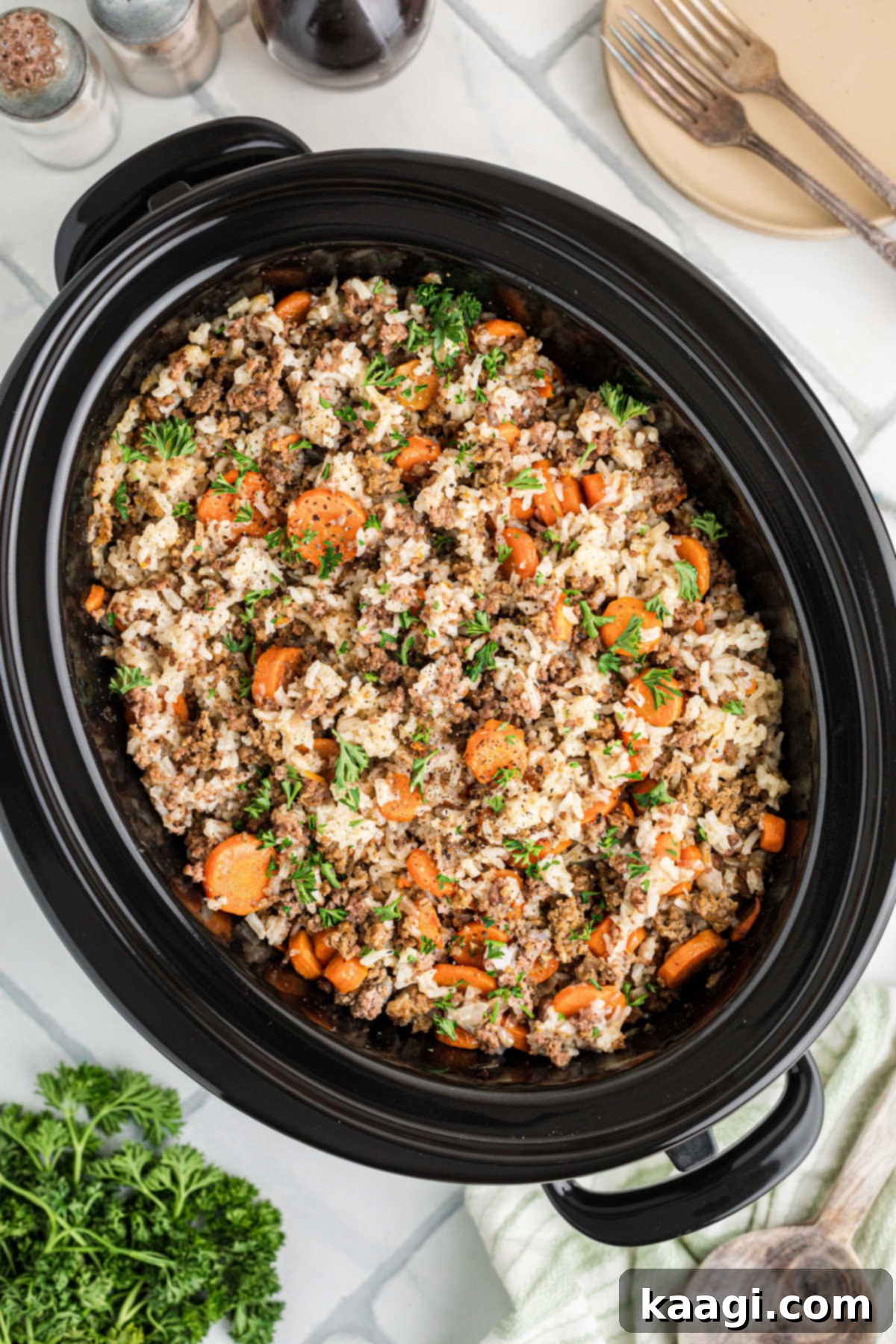 Overhead shot of a crock pot with carrots and ground meat, garnished with fresh parsley.