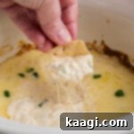 Chip being dipped into hot crab dip, made in the crock pot, highlighting its creamy texture.
