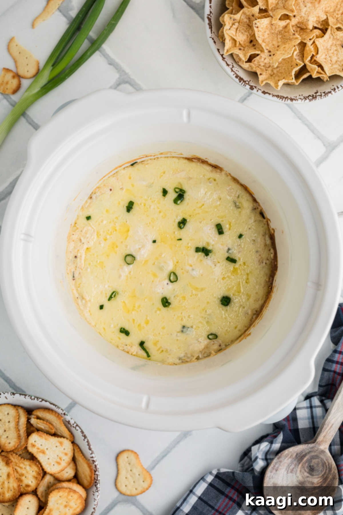 Overhead view of a crock pot with hot crab dip, beautifully garnished with fresh green onions.