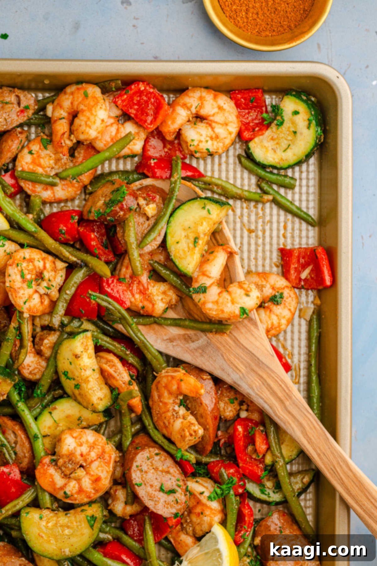 Cajun Shrimp and Sausage Sheet Pan Bake 5 Overhead shot of a sheet pan Cajun shrimp and sausage with a wooden spoon pushing through.