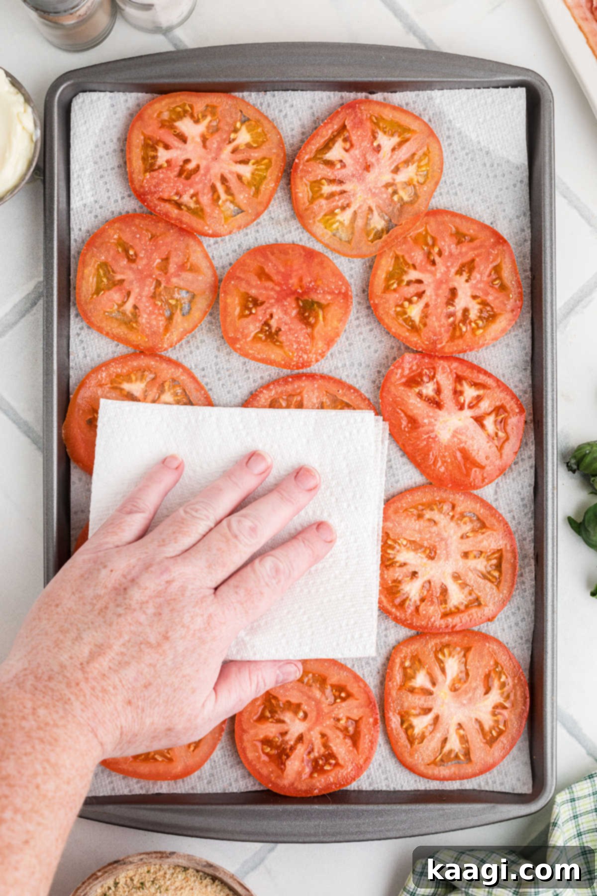 Dixie Tomato Tart 4 A baking sheet full of vibrant, sliced tomatoes being patted dry with paper towels to remove excess moisture.