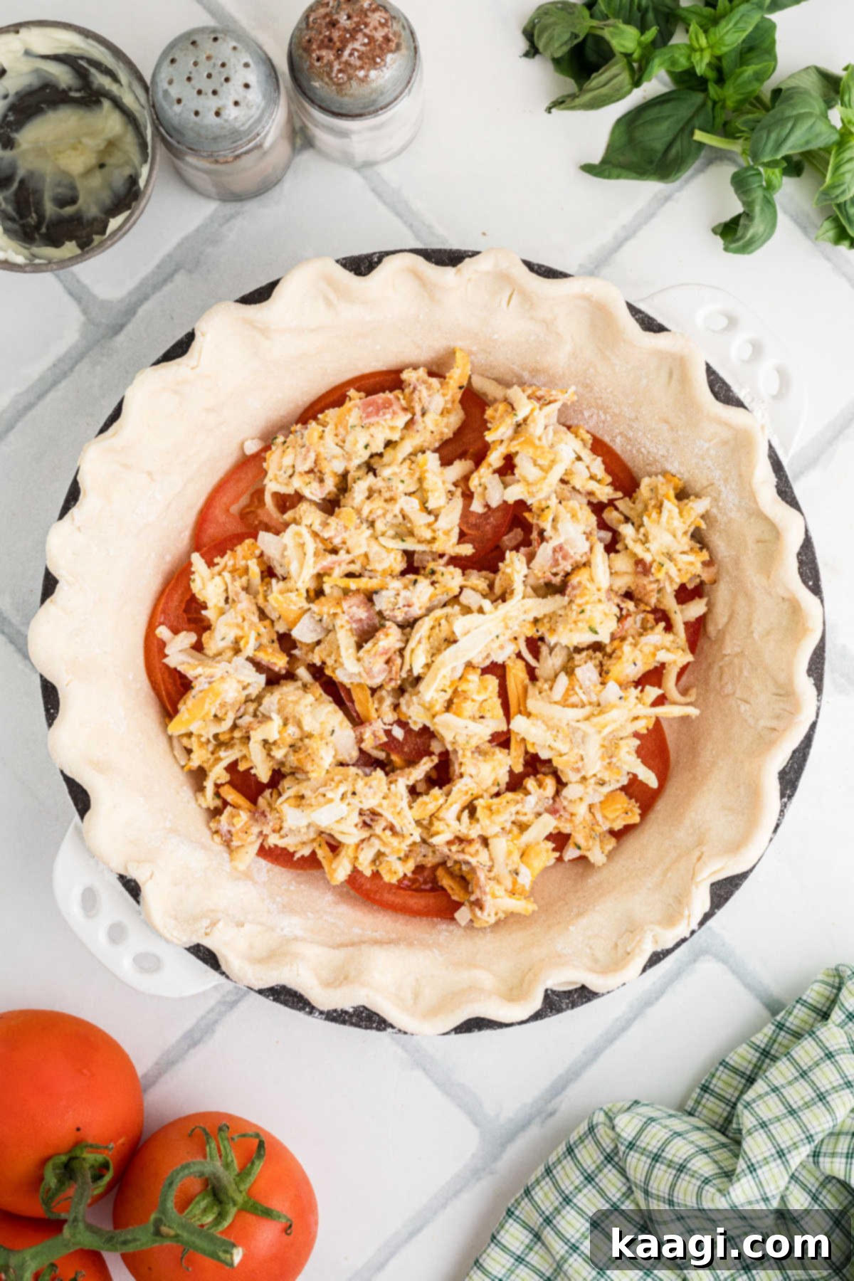 Dixie Tomato Tart 7 A creamy, cheesy mixture being carefully spooned and spread over the first layer of sliced tomatoes in a pie crust, preparing for the next layer.