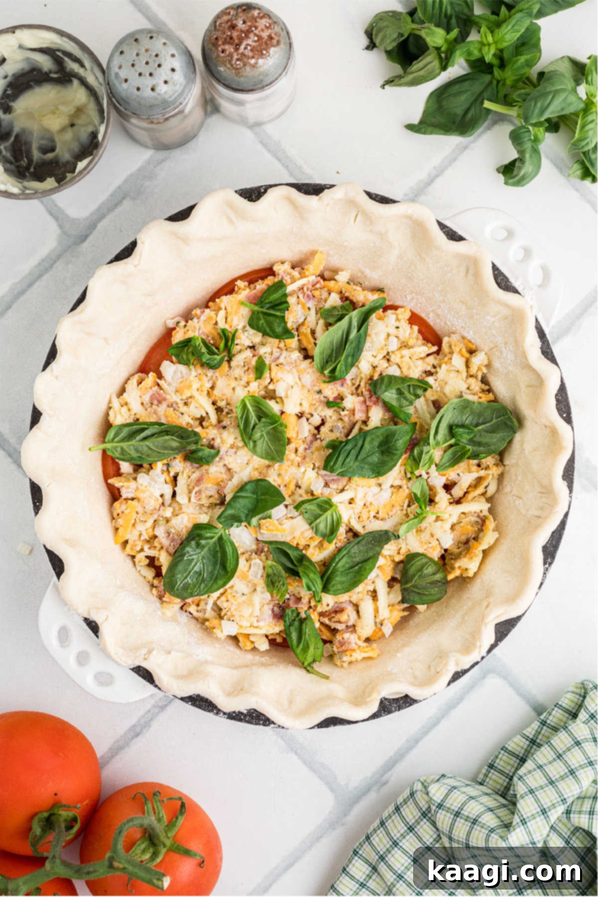 Dixie Tomato Tart 8 Fresh basil leaves artfully scattered over a partially assembled tomato pie, adding a burst of color and preparing it for the final layers.