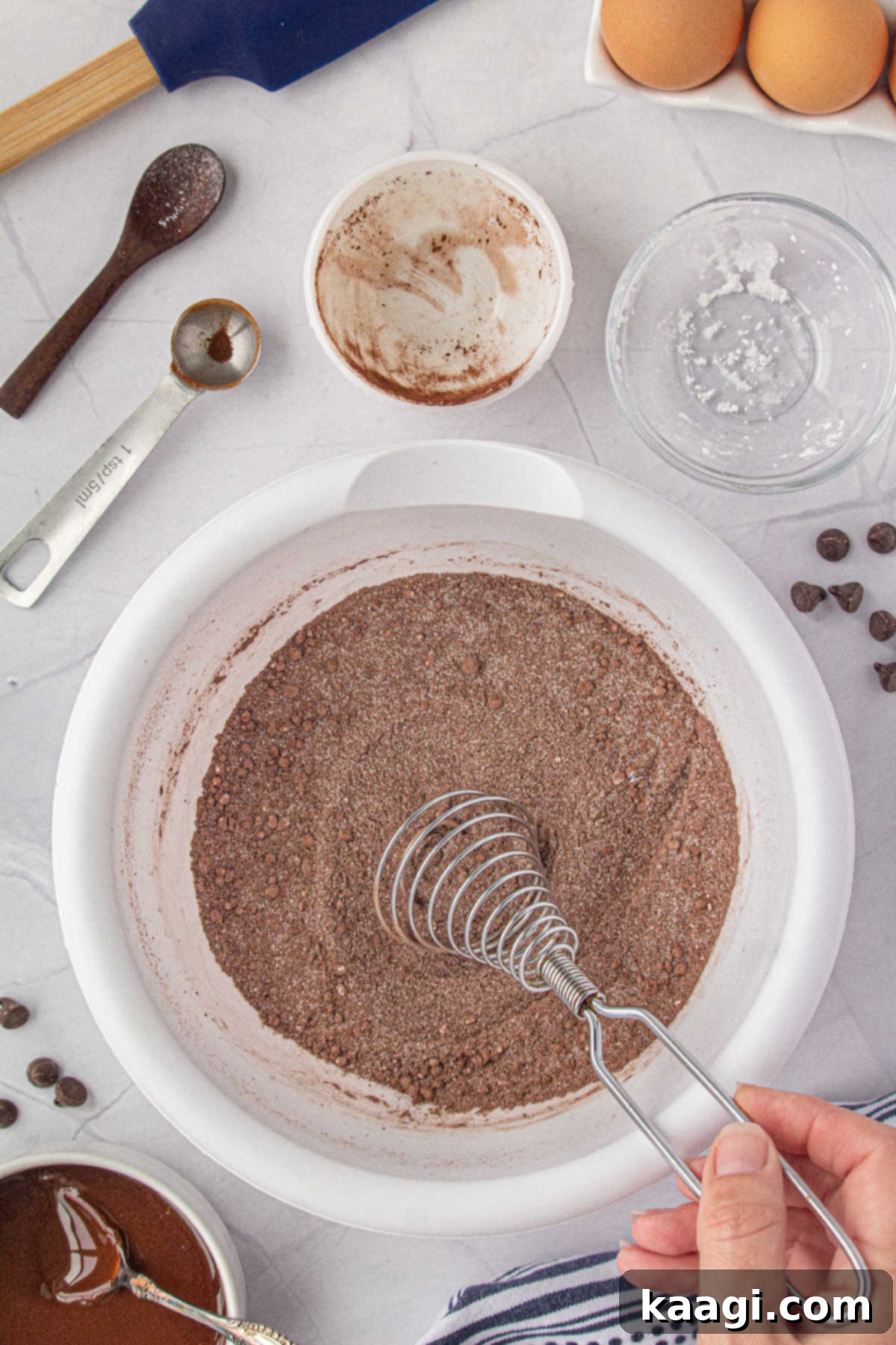 Various dry ingredients, including sugar and cocoa powder, are being expertly whisked together in a mixing bowl.