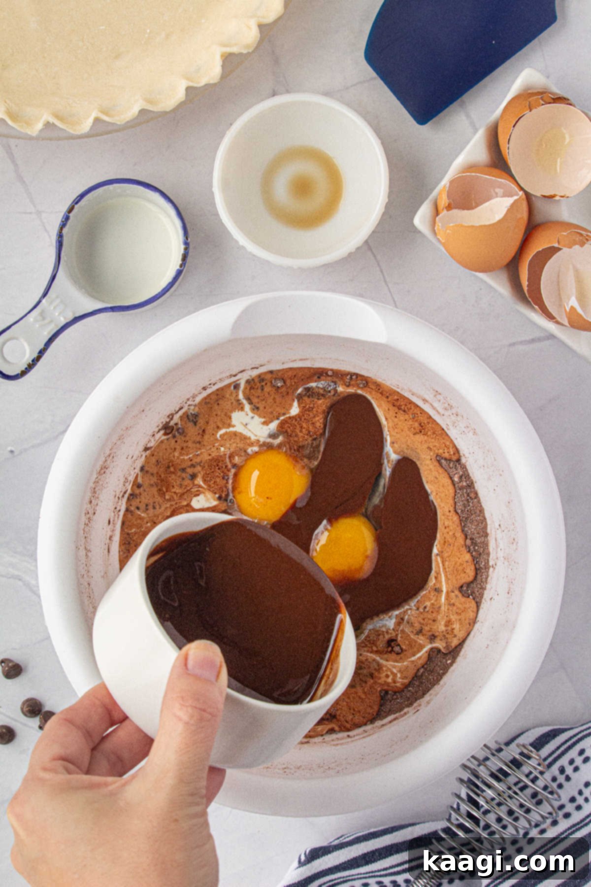 A stream of melted chocolate and butter is being poured into a bowl containing the dry ingredients for the pie filling.