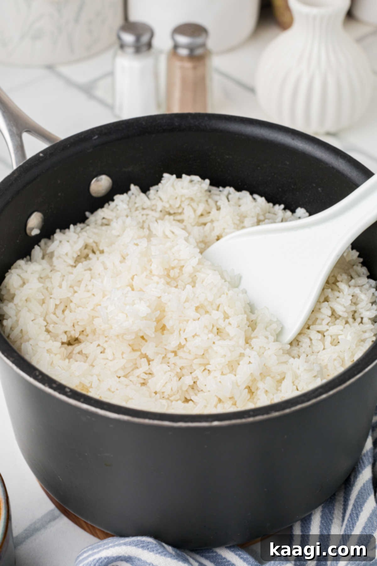 A pot of perfectly cooked, fluffy white rice with a serving spoon.