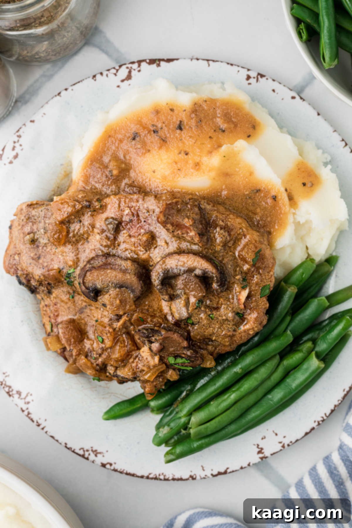 Overhead shot of a plate of smothered pork chops on some mashed potatoes with some green beans.