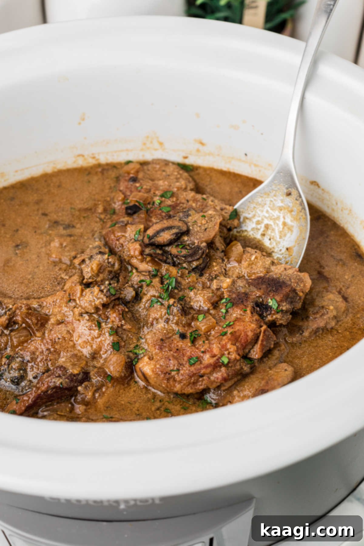 A crock pot smothered pork chops recipe with a spoon digging in.