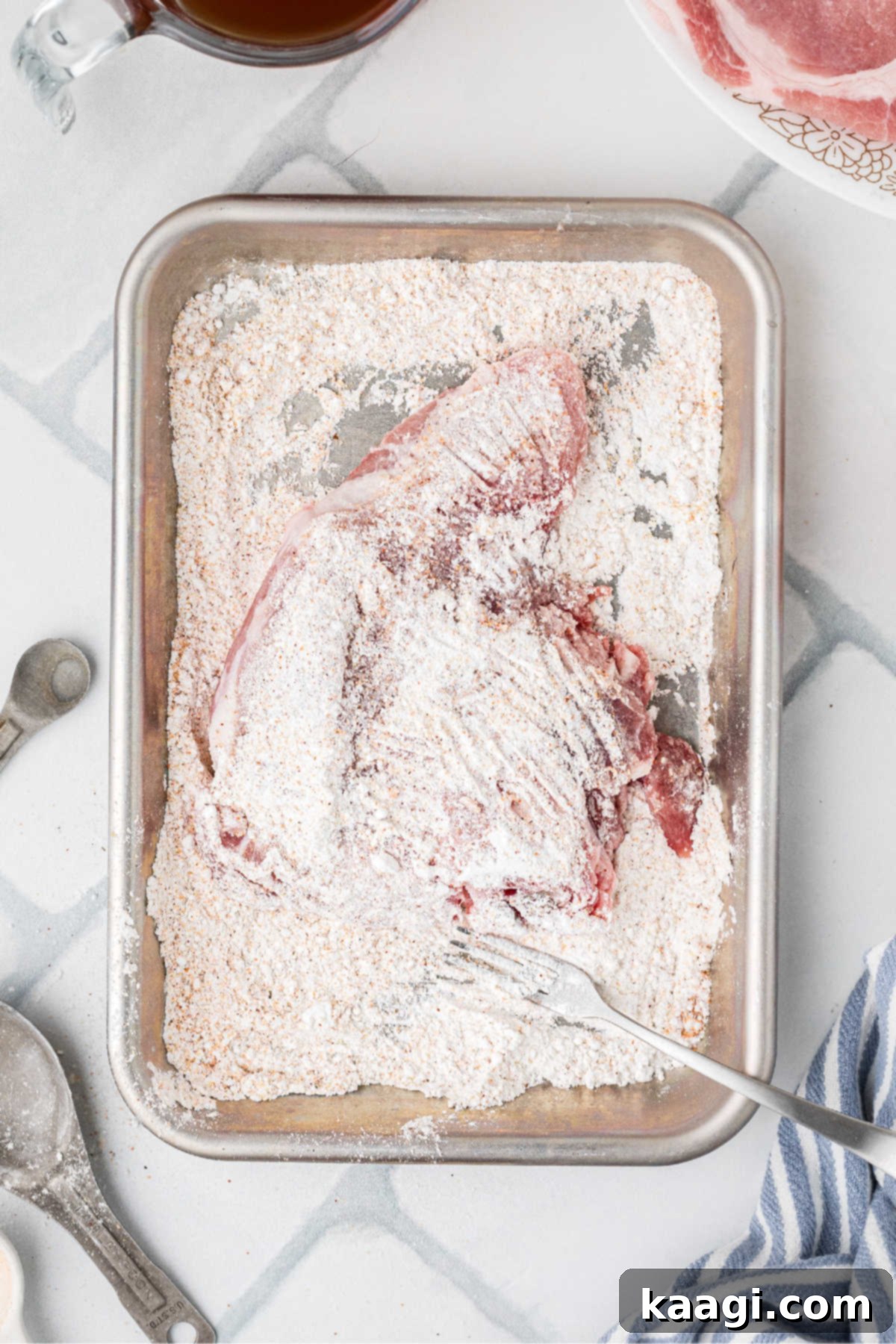 A pork chop being passed through a flour seasoning mixture.