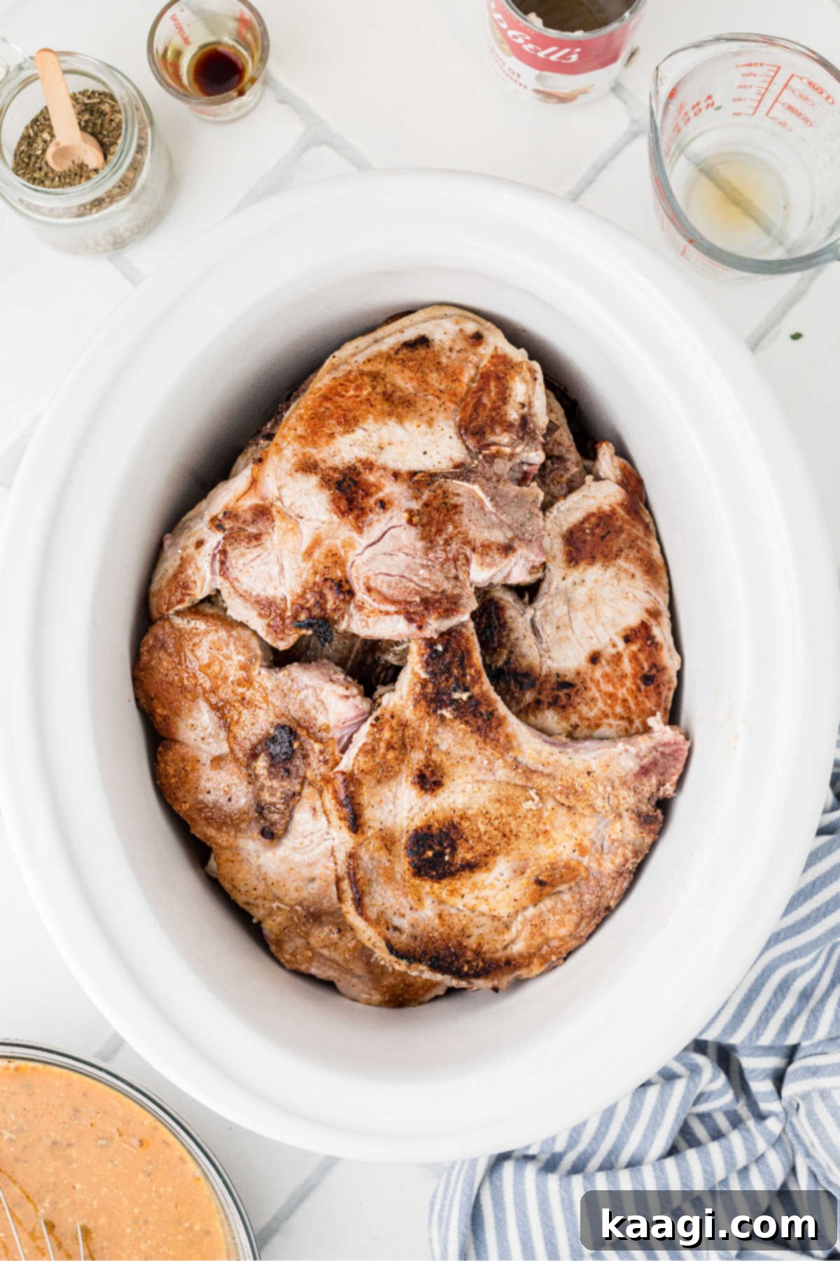 A slow cooker with seared pork chops.
