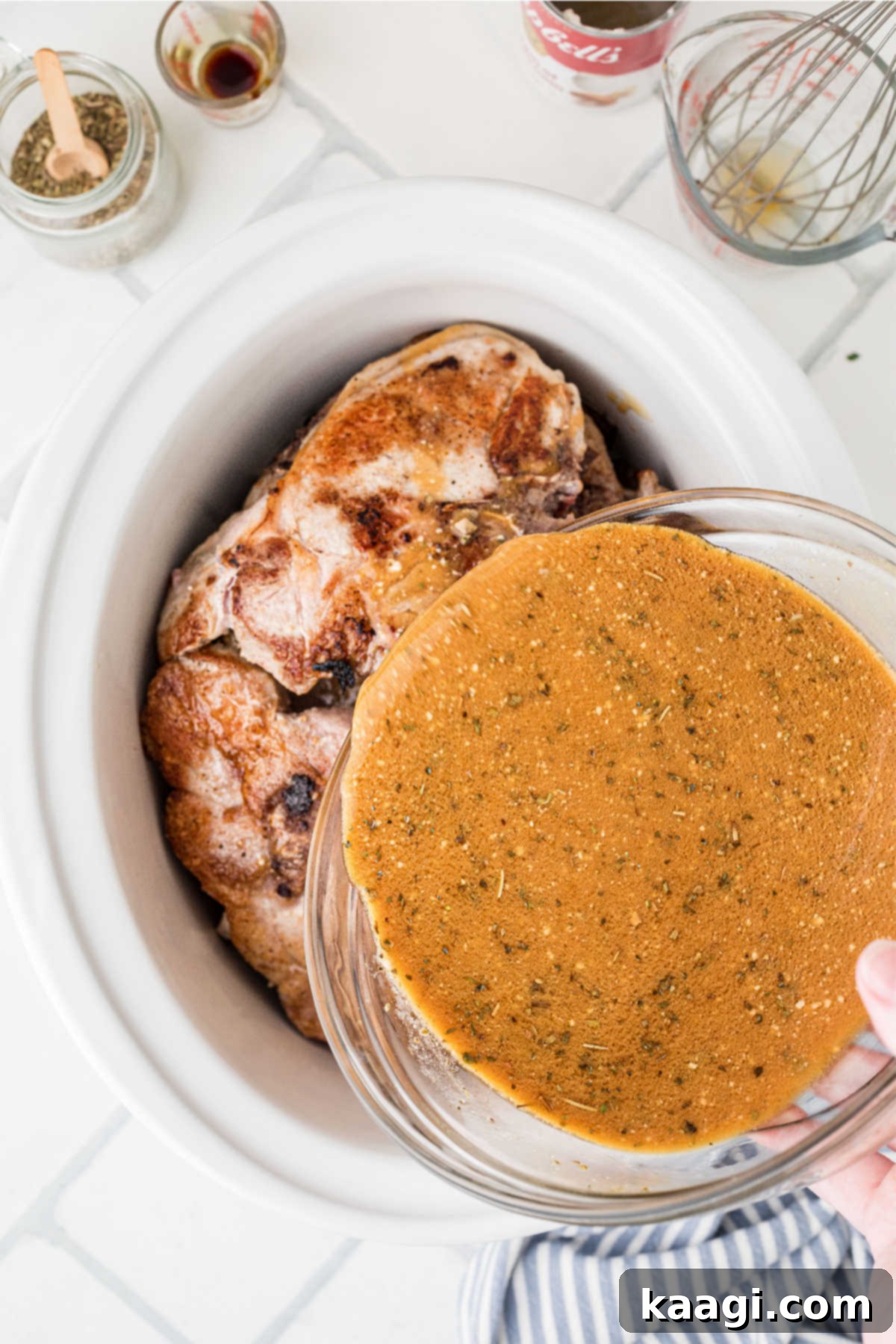 A large slow cooker with pork chops, a gravy is being poured over the top.