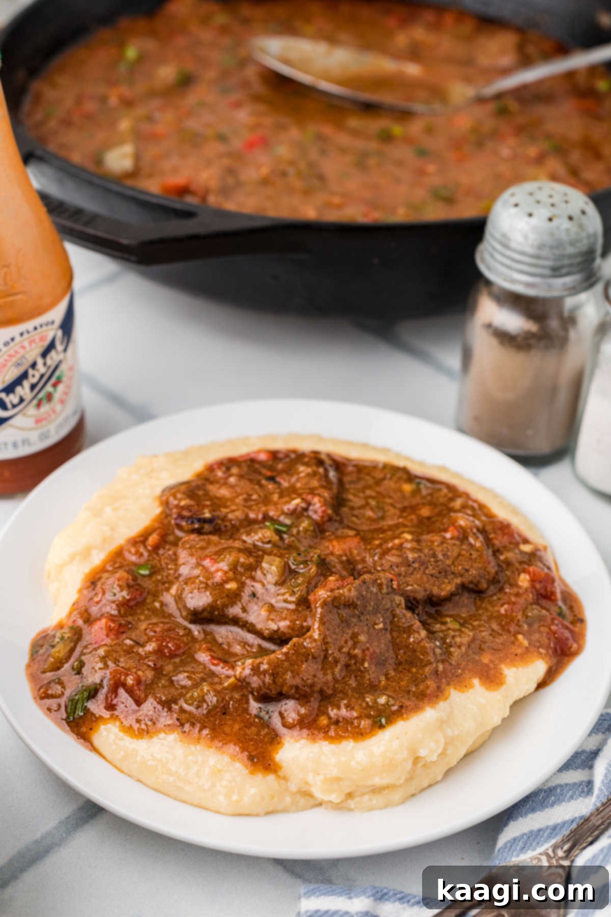 A plate full of cheesy grits and grillades poured on top. There's a skillet in the background.