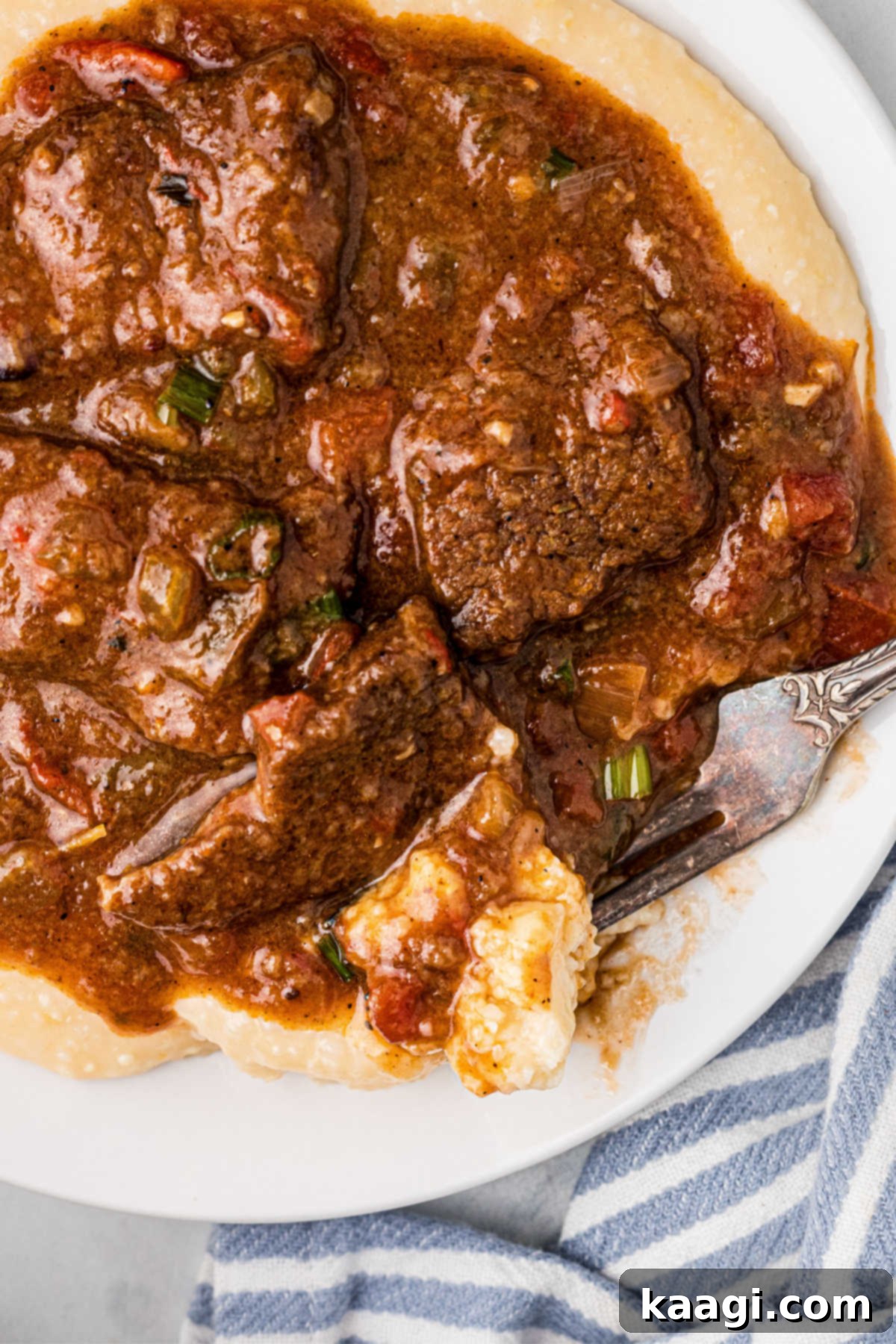 Very close up image of a plate full of grillades and grits, with a fork digging in.