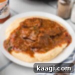 Close up of a plate of grillades and grits, the image has been cropped square.